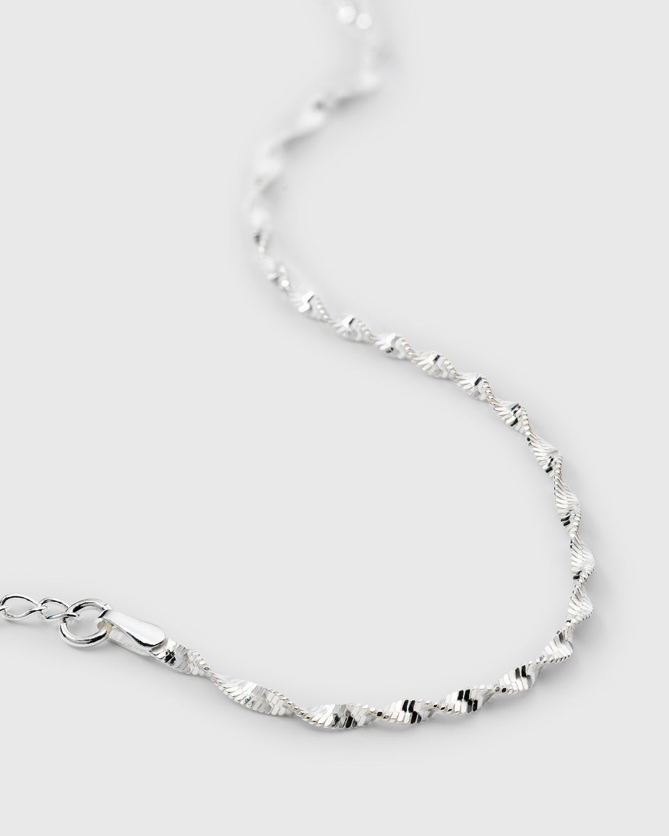 A close-up product shot of a delicate, twisted herringbone bracelet in sterling silver, showing its shimmering, textured pattern and clasp.