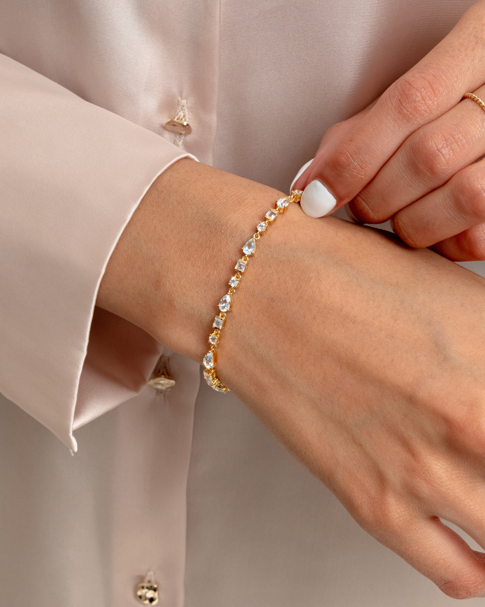 A close-up of a model wearing the Pam Bracelet in gold, showcasing its delicate design of variously shaped white topaz stones on her wrist.