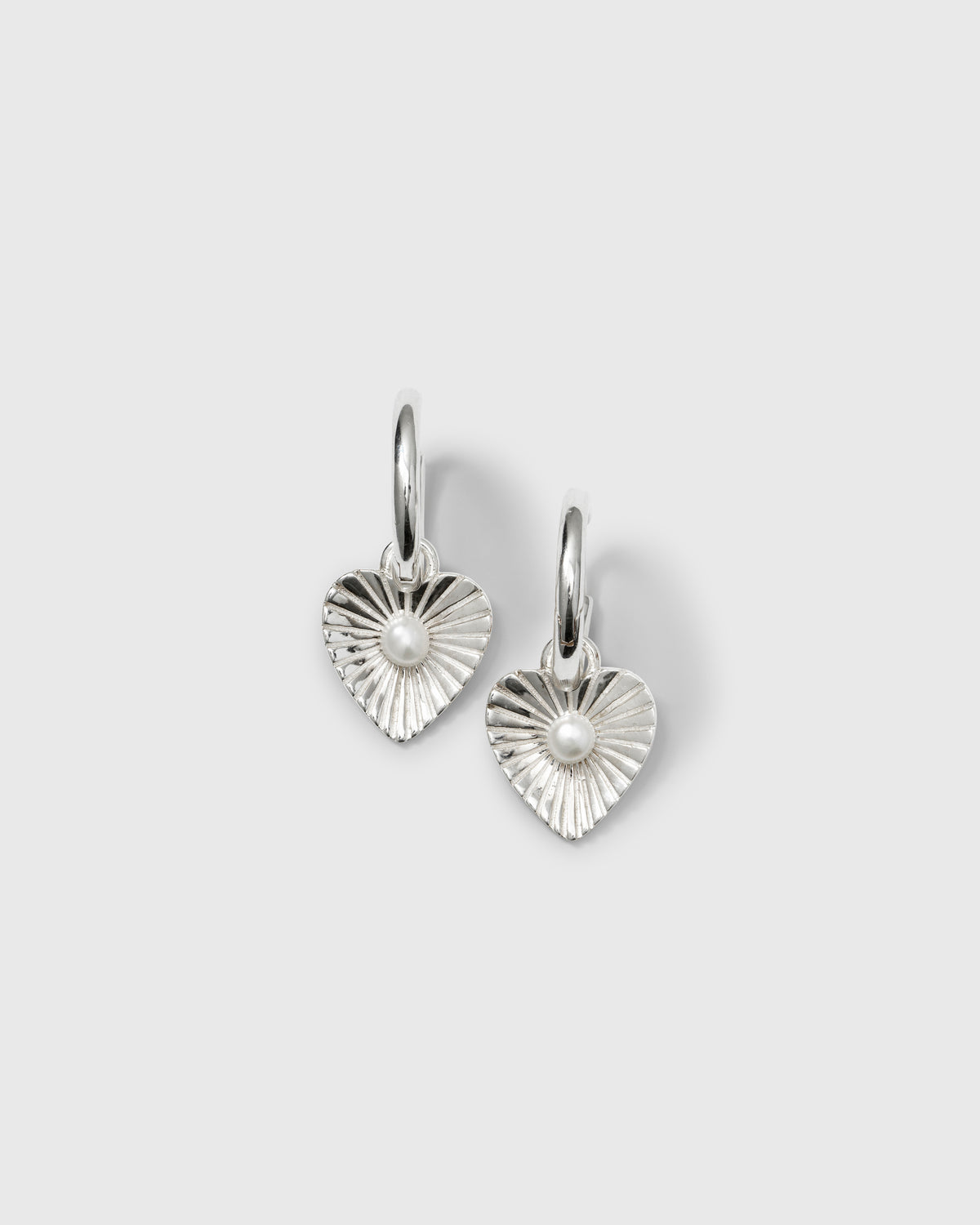 A product shot of the Aurelia Earrings in silver, featuring hoop earrings with a textured, heart-shaped pendant and a small freshwater pearl at its center.