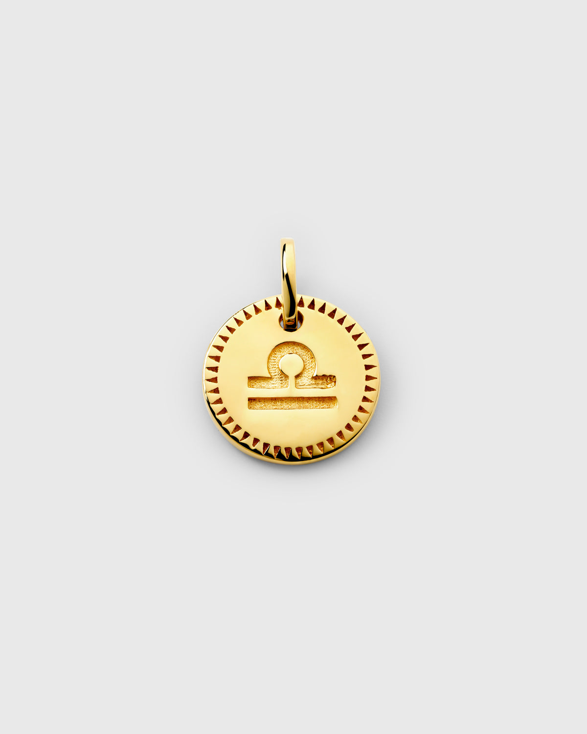 A close-up of the gold Beloved Zodie Pendant, showcasing the engraved Libra zodiac symbol on the circular charm, framed by a textured border.