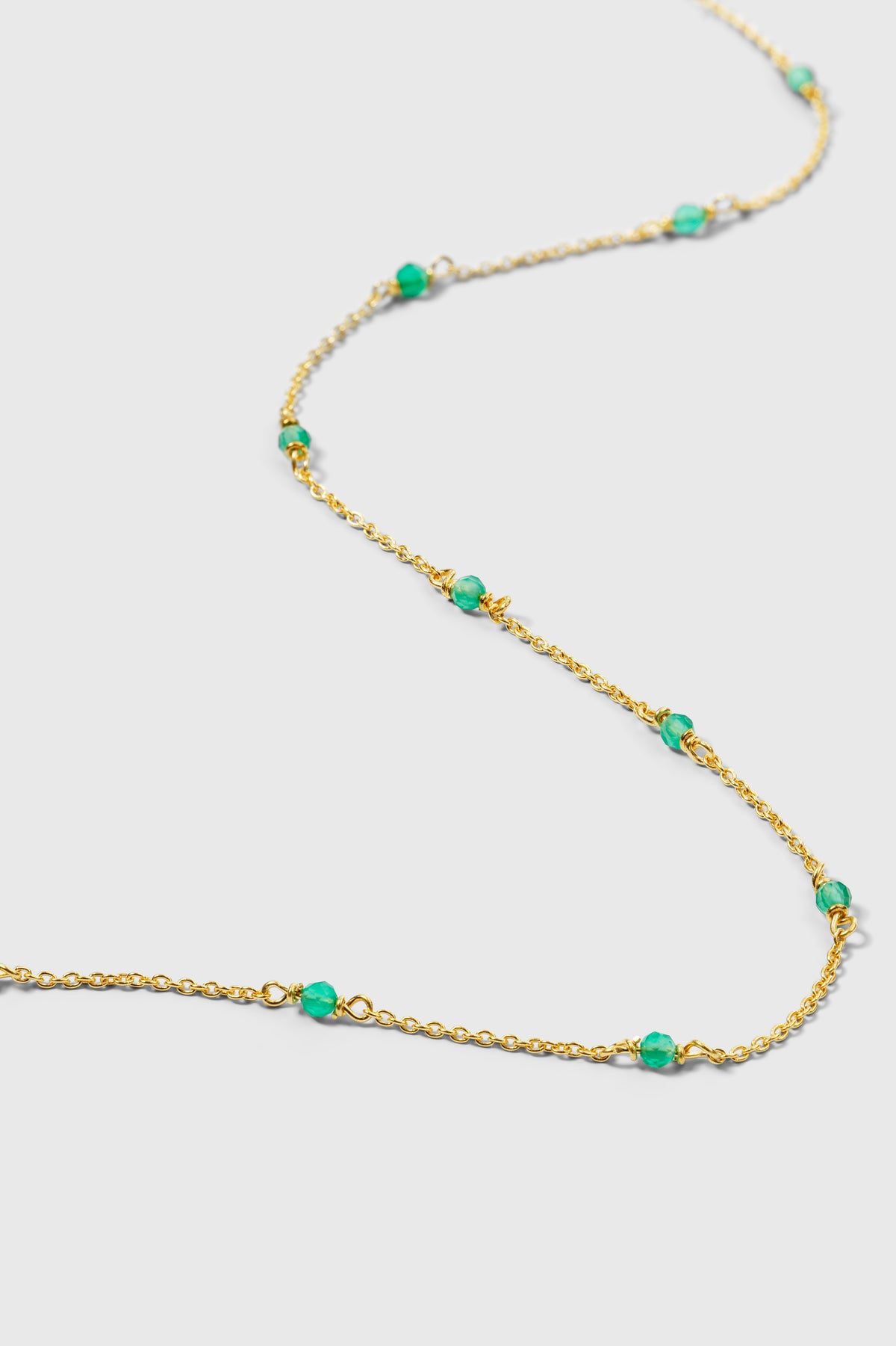 A product shot of the Santa Monica Necklace in gold, laid out in a wavy line to show its fine chain design adorned with vibrant green onyx stones.