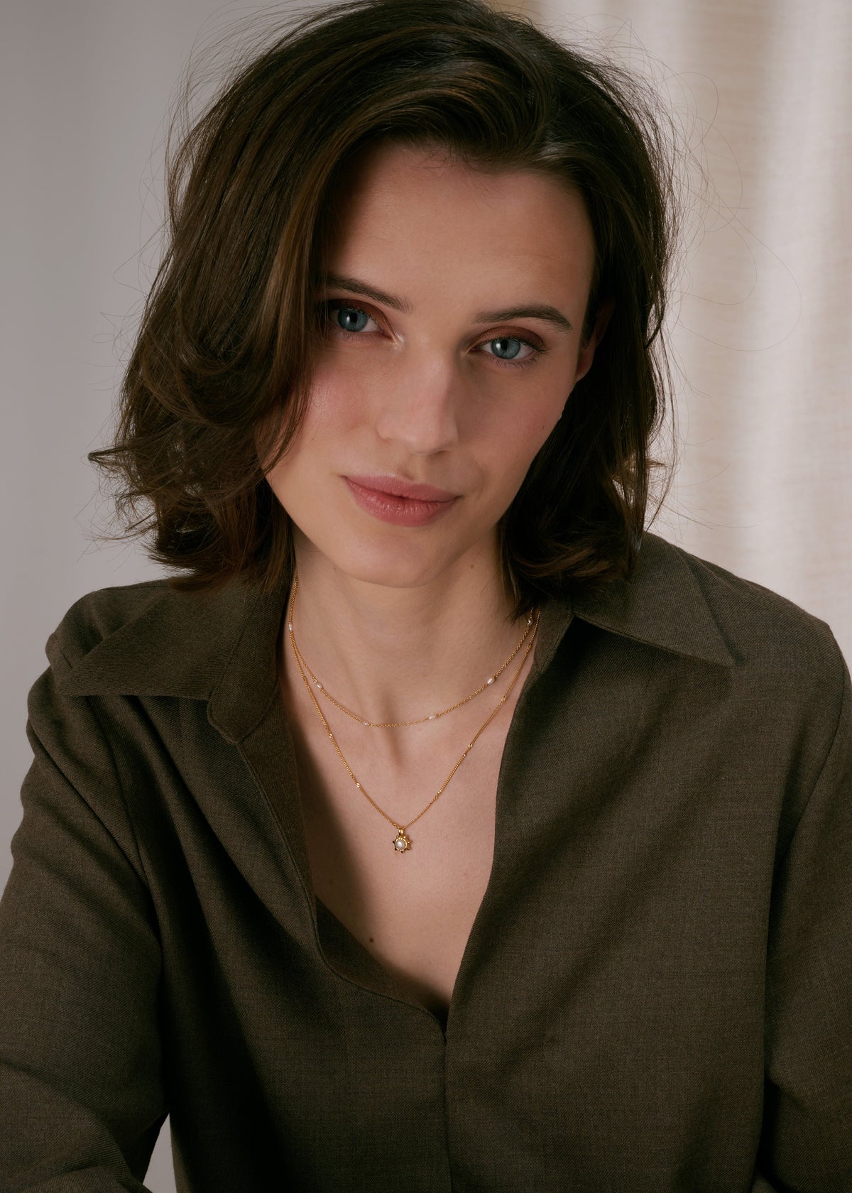 Two layered gold necklaces: a delicate chain with small spaced freshwater pearls, and a second chain with a sunburst pendant featuring a pearl in the center.