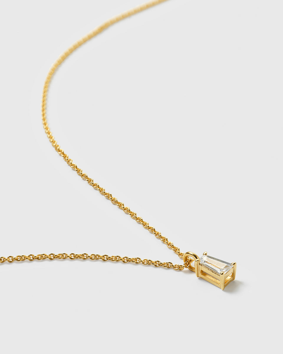 A close-up product shot of the Iggy Necklace in gold, showing its fine chain and a pendant with a tapered baguette-cut cubic zirconia.