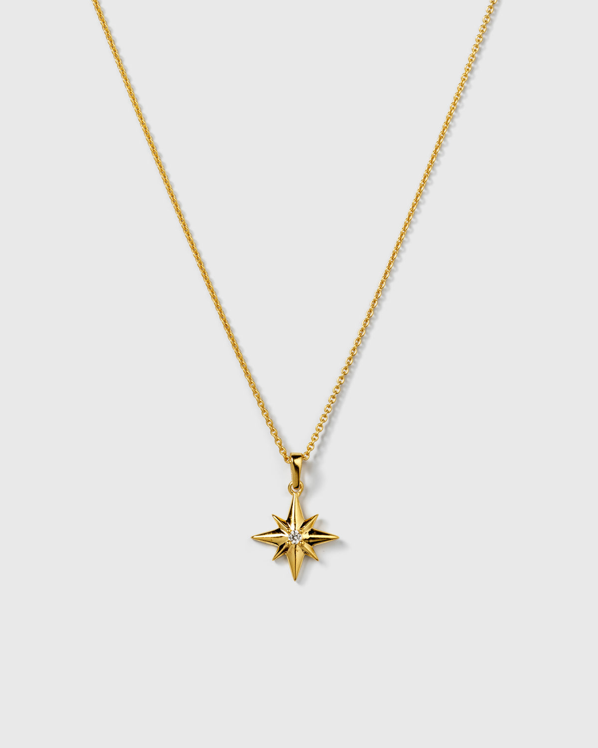 A product shot of the North Star Big Necklace in gold, featuring a fine chain and an eight-pointed star pendant with a sparkling crystal at its center.
