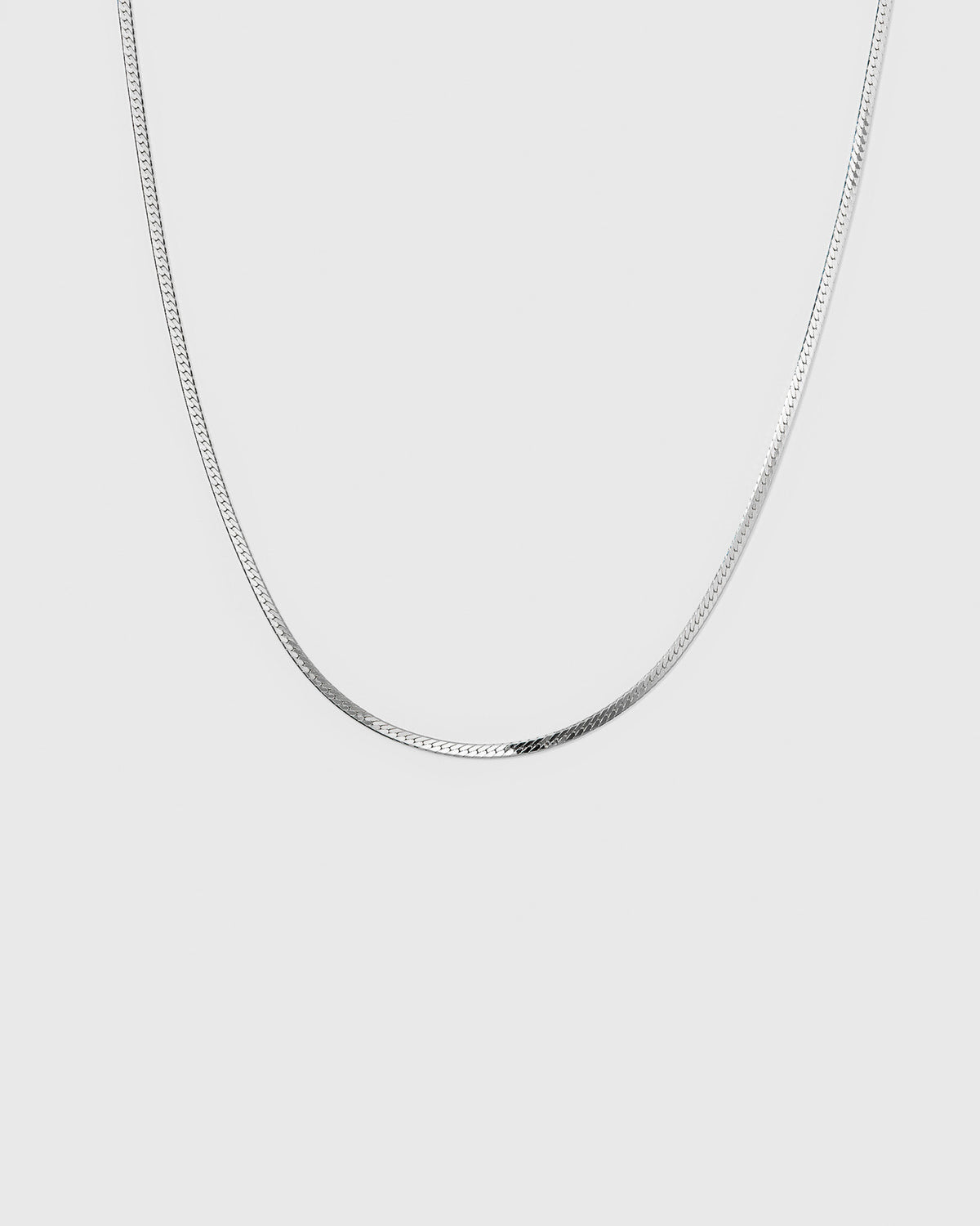 A product shot of the Herringbone Necklace in silver, highlighting its smooth and flat chain design.