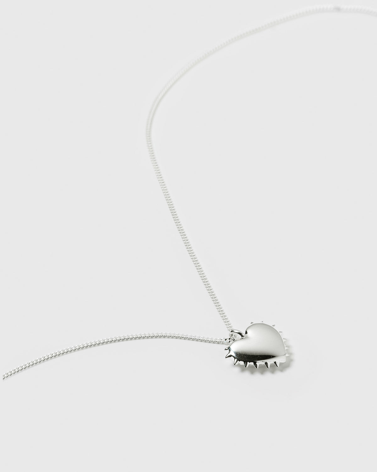 A product shot of the True Love Spike Heart Necklace in silver, laid out to display its fine chain and heart-shaped pendant with a spiky border.
