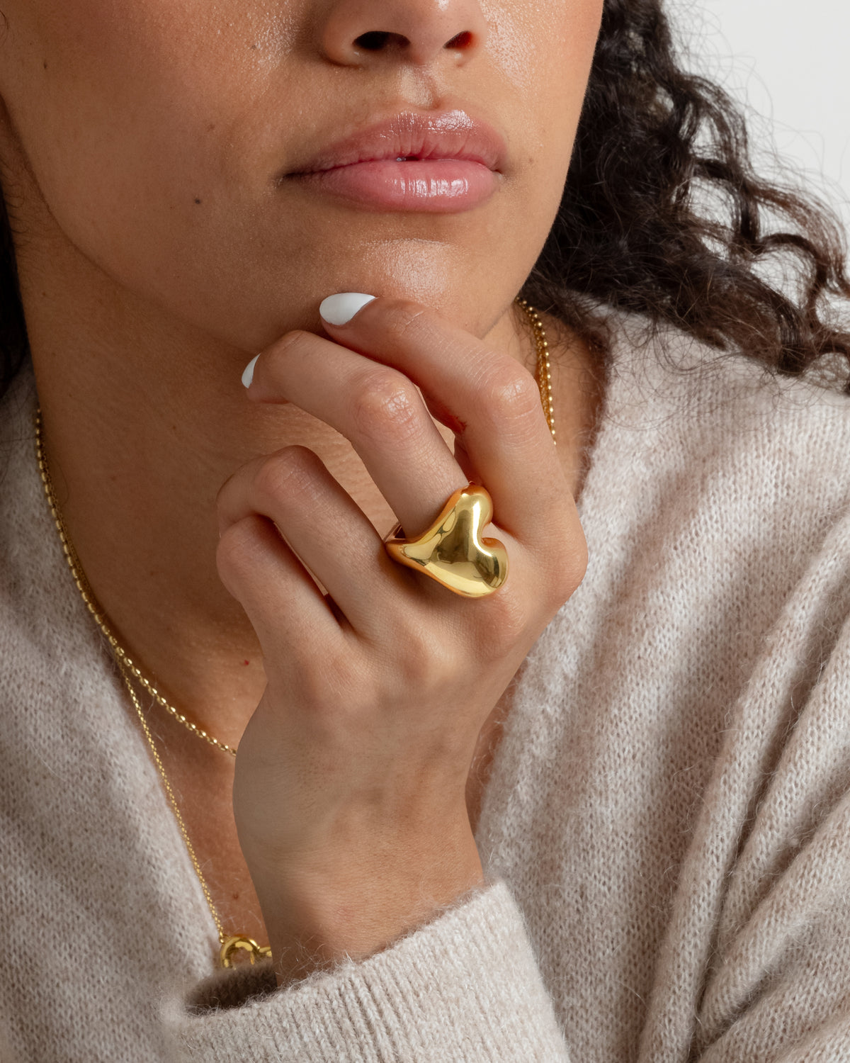 A close-up of a model wearing the Bolded Heart Ring in gold, a large and shiny heart-shaped design, styled with a simple gold chain necklace.