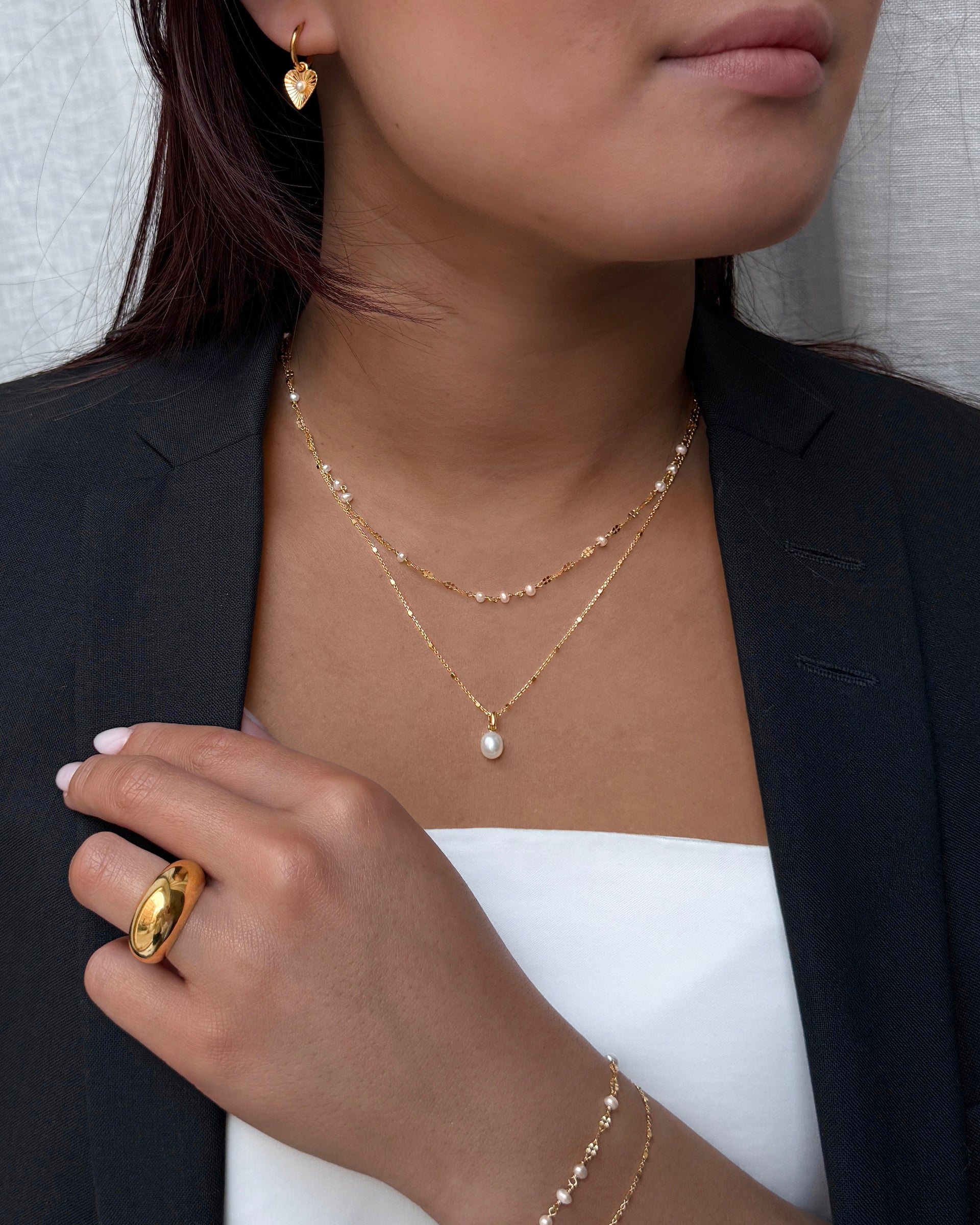 A shorter gold necklace with several small pearls on it together with a longer necklace with small gold studs on it and a pearl charm. And a large gold ring. 