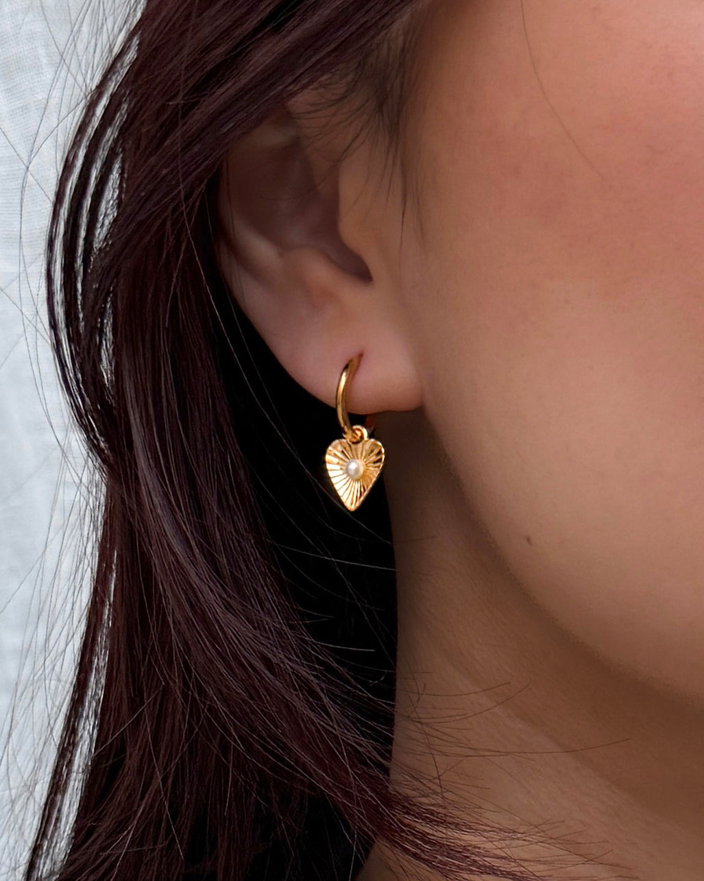Golden earring shaped like a heart with a small freshwater pearl in the middle