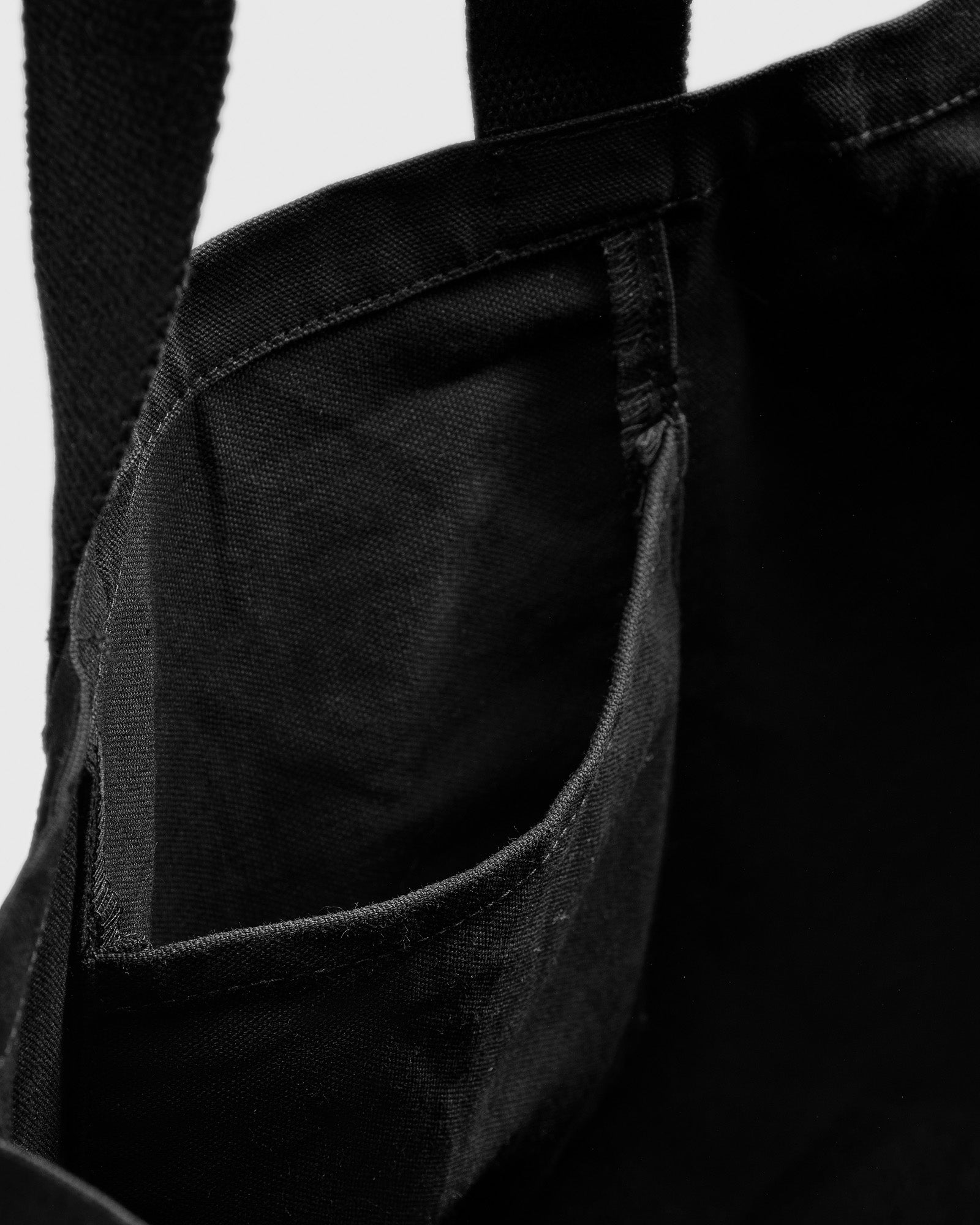 A detailed view of the small inner pocket inside the black cotton Syster P Tote Bag.