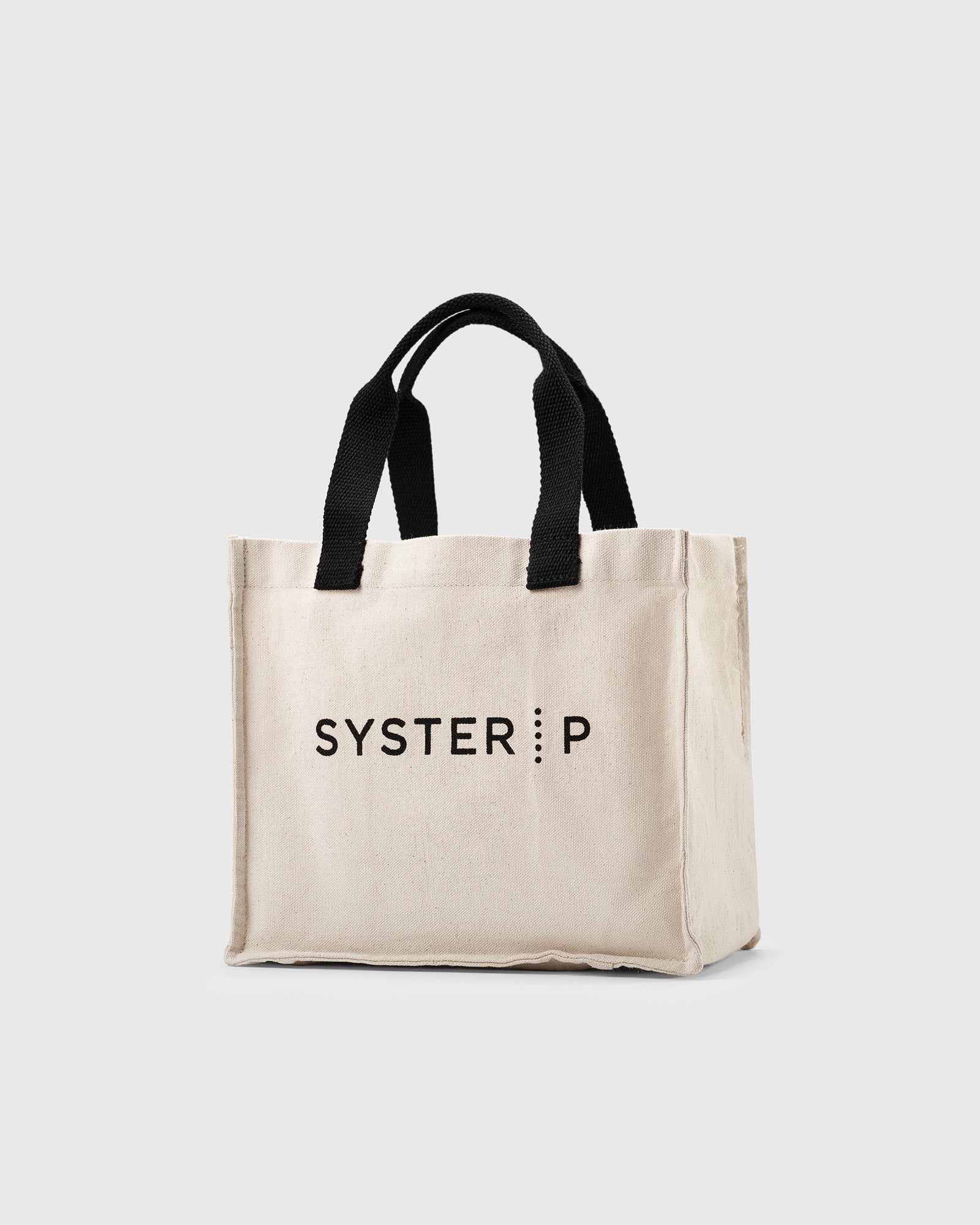 A product shot of the Syster P Lunch Tote, a beige cotton bag with black handles and the brand's logo printed on the front.