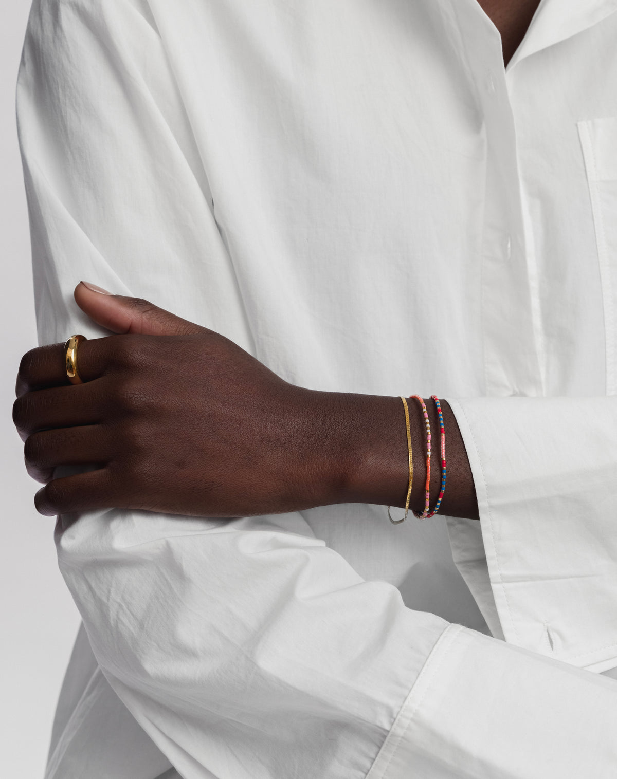 A model wearing the Code Bracelet Gold 'Keep Going', styled in a stack with another multicolored beaded bracelet and a thin gold snake chain bracelet, complemented by a simple gold ring on her thumb.