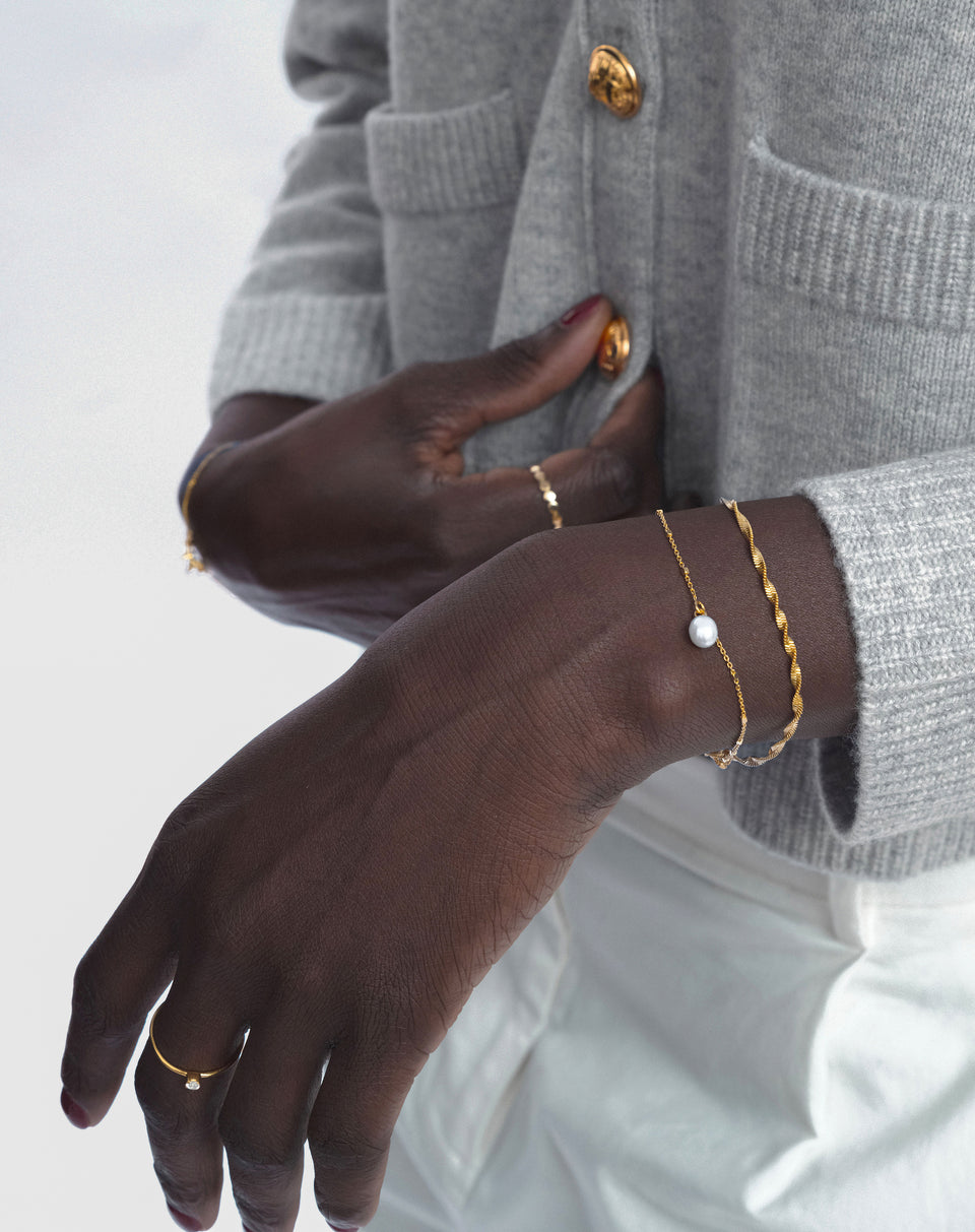 A model wears the Treasure Single Pearl Bracelet in gold, styled alongside a twisted gold chain bracelet and two delicate gold rings.