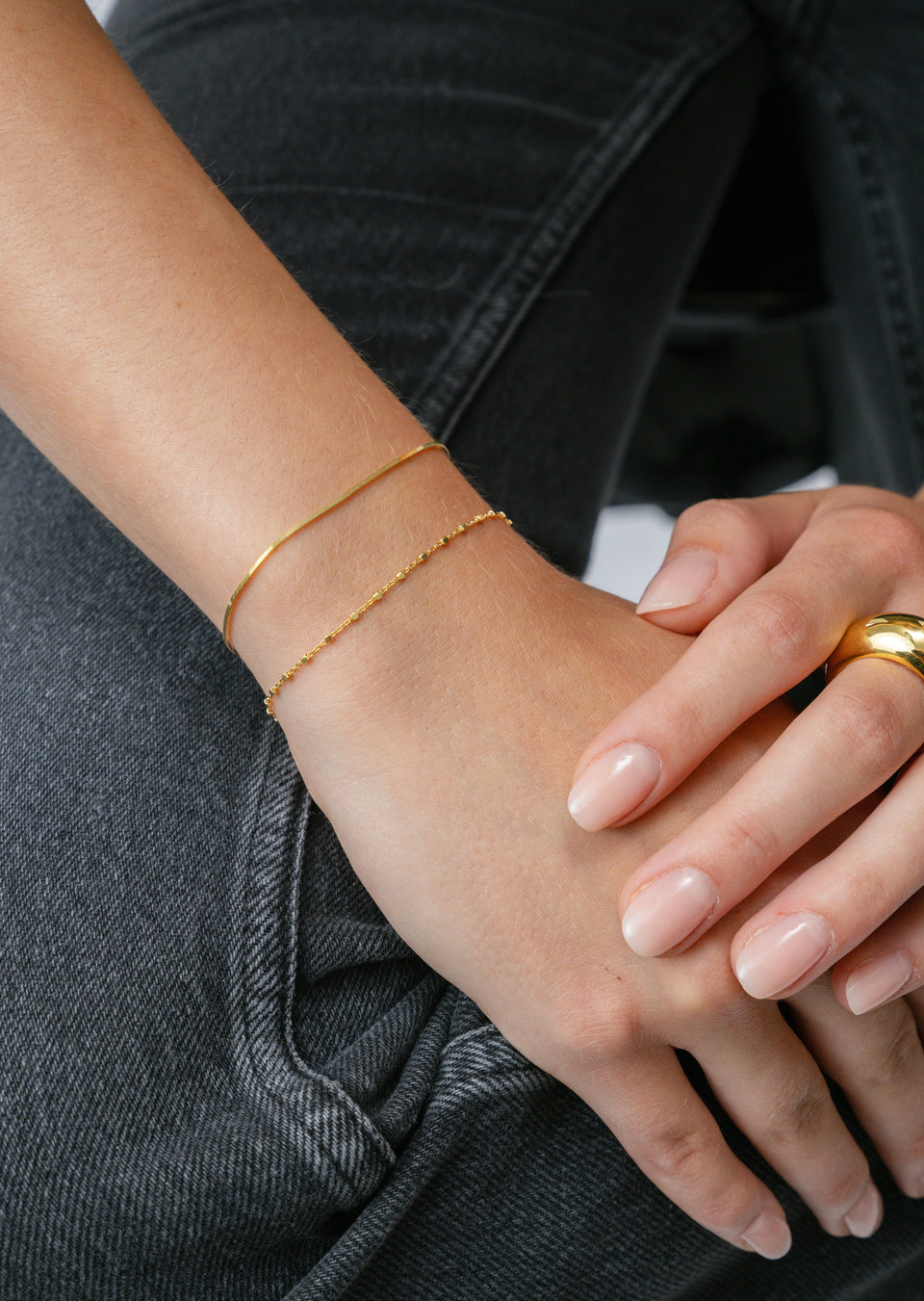 A model wearing the Sheer Station Bracelet in gold, stacked with a thin gold snake chain bracelet and paired with a chunky gold dome ring.