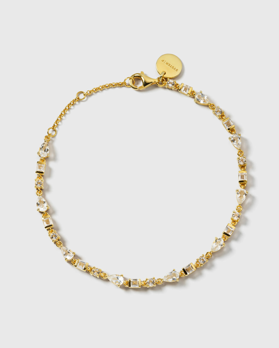 A product shot of the Pam Bracelet in gold, laid out in a circular shape to showcase its delicate chain set with sparkling white topazes in various shapes.
