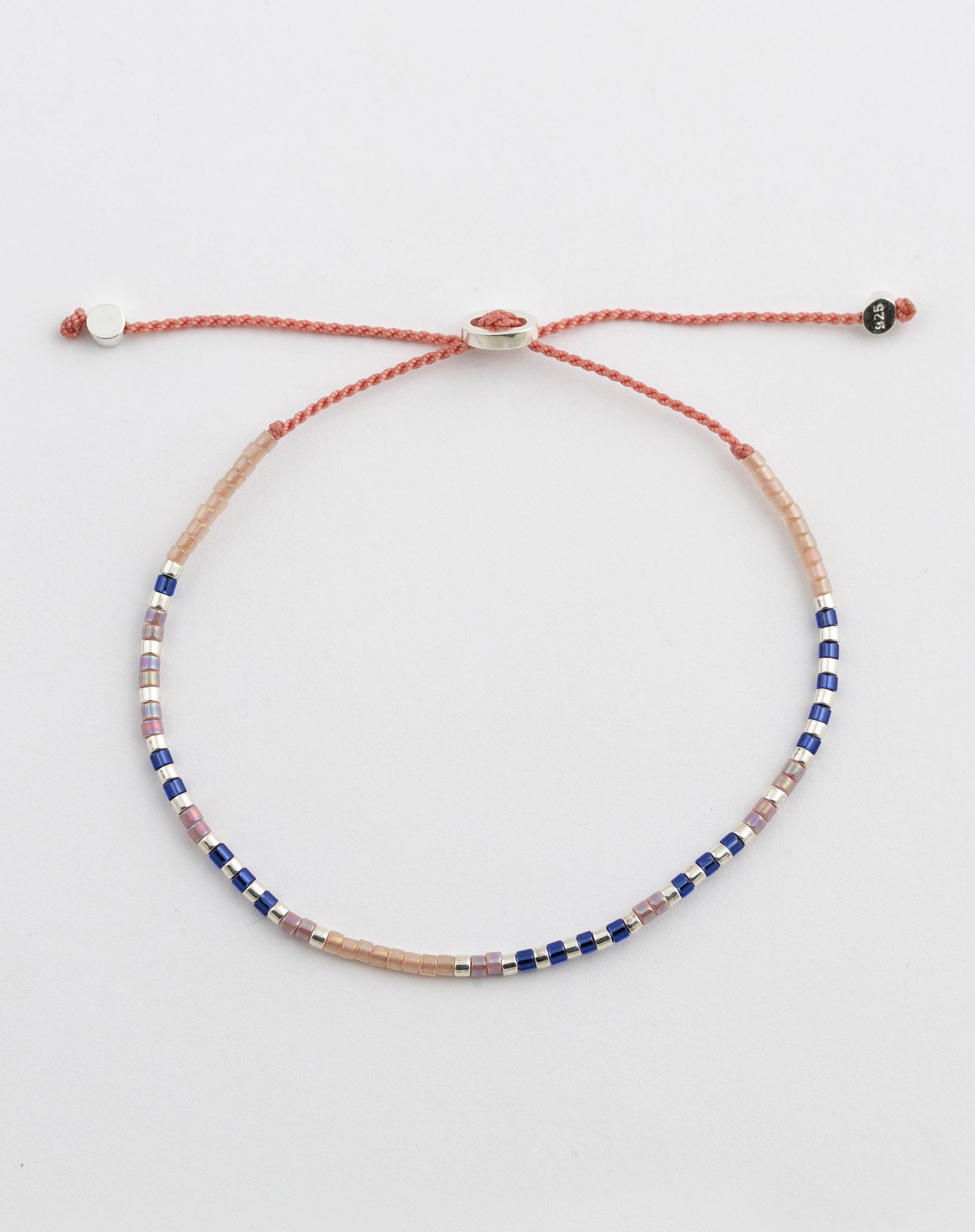 A product shot of the Code Bracelet Silver Just Breathe, laid out in a circle to show its morse code design of blue, pink, and silver glass beads on an adjustable pink cord.