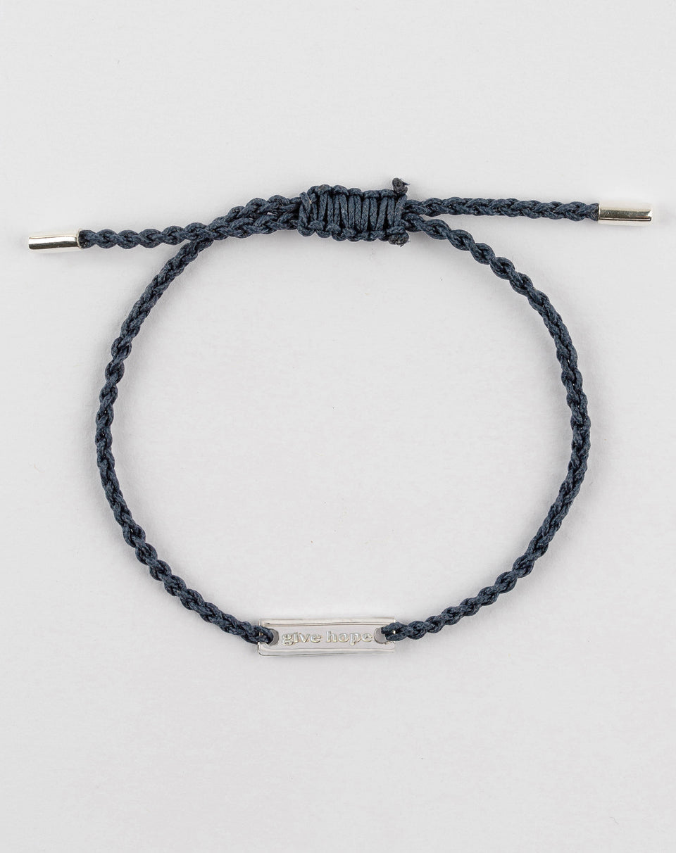 A product shot of the Give Hope bracelet in navy, featuring a braided cord and a sterling silver plaque engraved with the words 'give hope'.