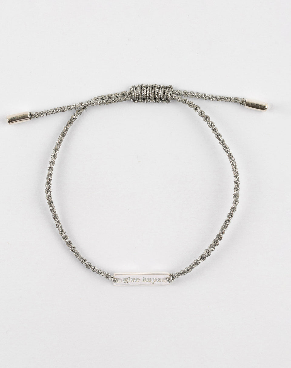 A product shot of the Give Hope bracelet in silver metallic, laid out in a circle. It features a braided metallic thread and a central silver plaque engraved with the words 'Give Hope'.