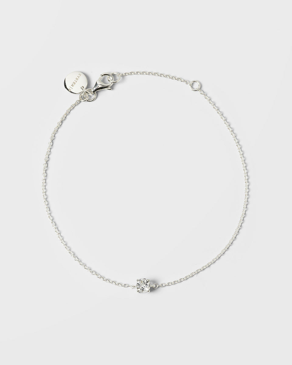 A product shot of the Minimalistica Solo Nova Bracelet in silver, laid out in a circle to show its design of a delicate chain with a single, central white topaz stone.