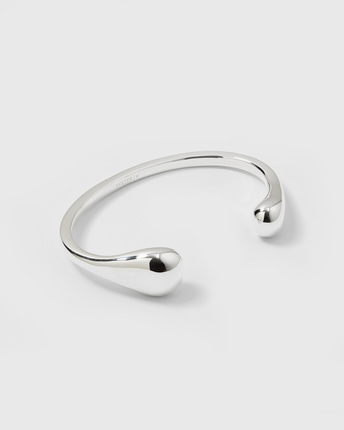 A product shot of the Bolded Drops Bangle in silver, showcasing its open cuff design with smooth, bulbous ends shaped like drops.