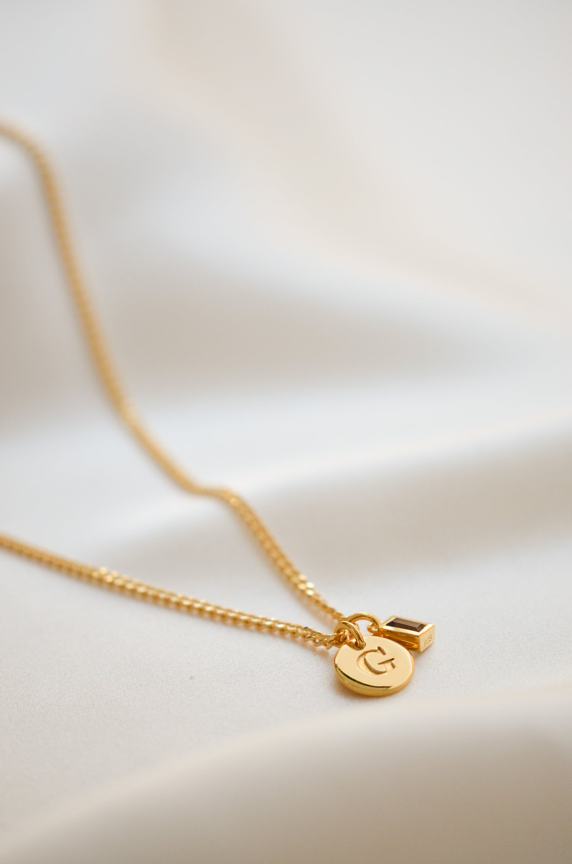 Gold chain with a smal gold letter and a gold pendant with a brown onyx