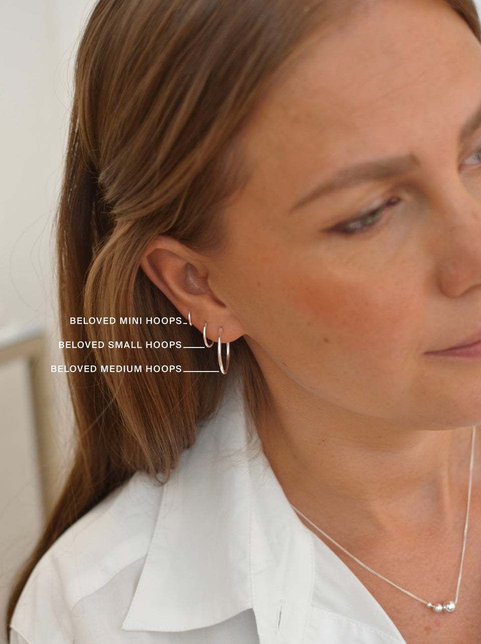 A size guide image showing a model wearing the Beloved Mini, Small, and Medium hoops in silver to compare their sizes.