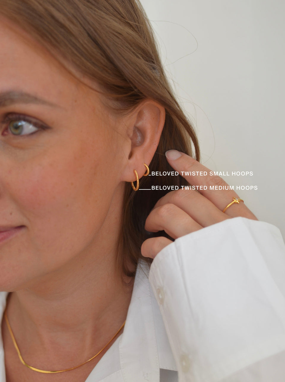 A close-up of a model wearing the Beloved Twisted Medium and Small Hoops in gold, paired with a delicate gold ring and a gold snake chain necklace.