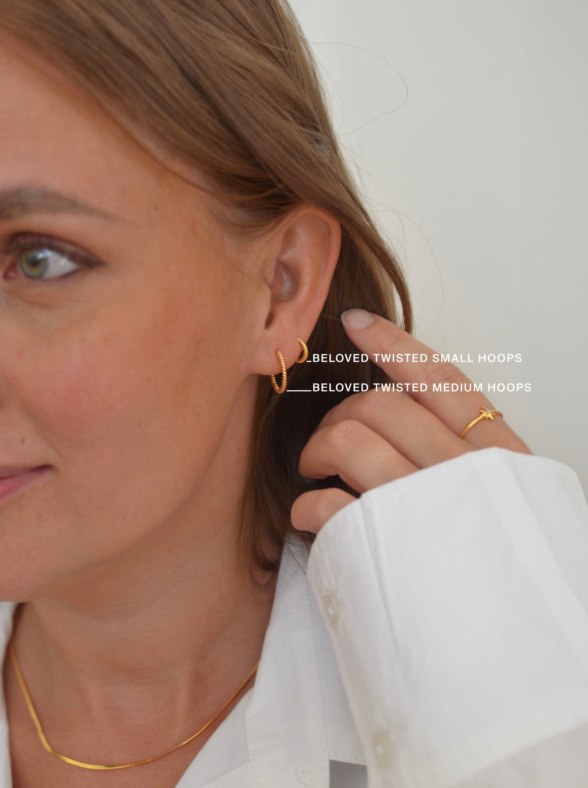 A close-up shot of a model wearing the gold Beloved Twisted Small Hoops and the Beloved Twisted Medium Hoops, a gold snake chain necklace, and a star-shaped gold ring.