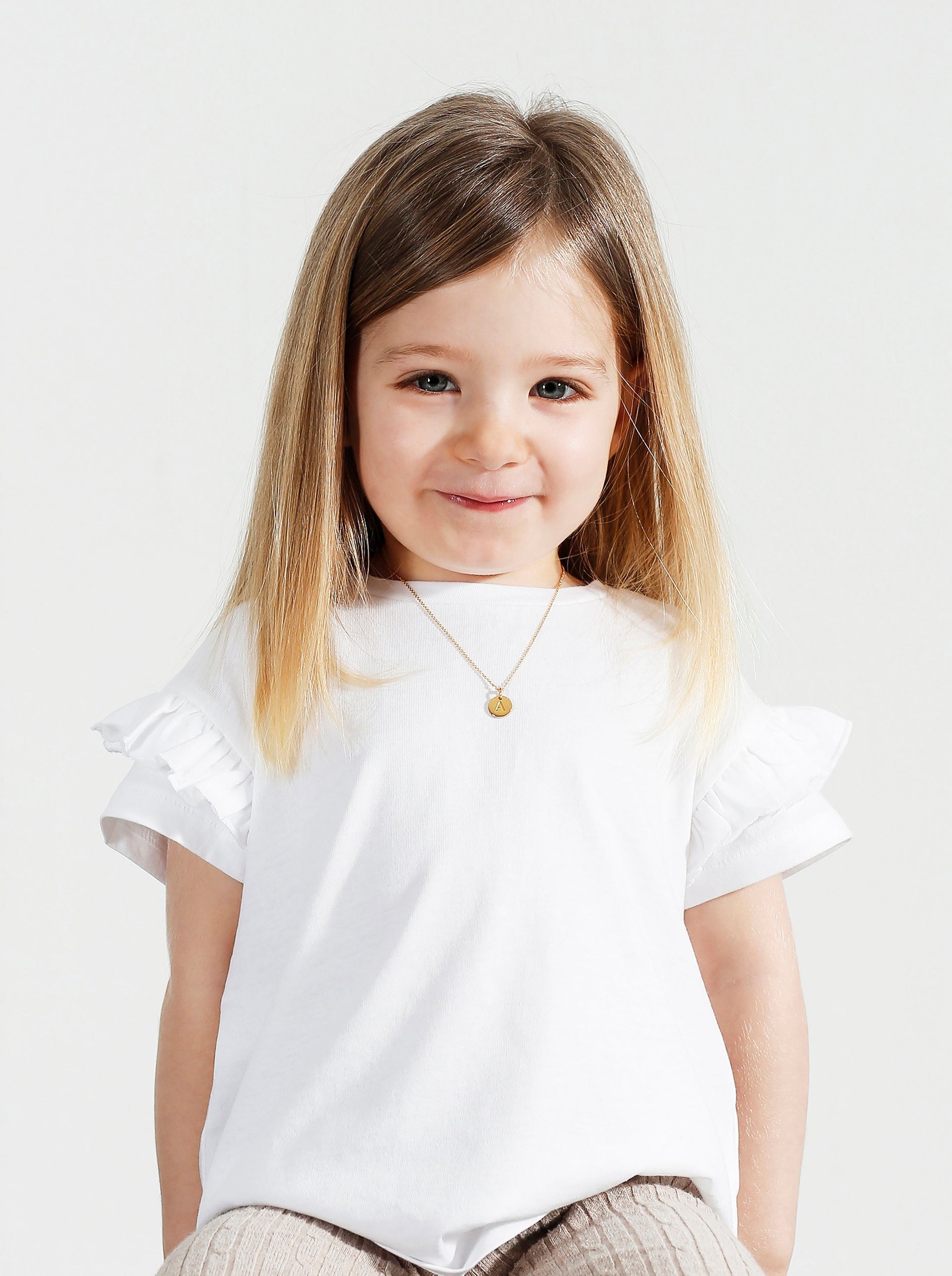 A young girl models the Beloved Baby Chain in gold, styled with a small, round letter A pendant.