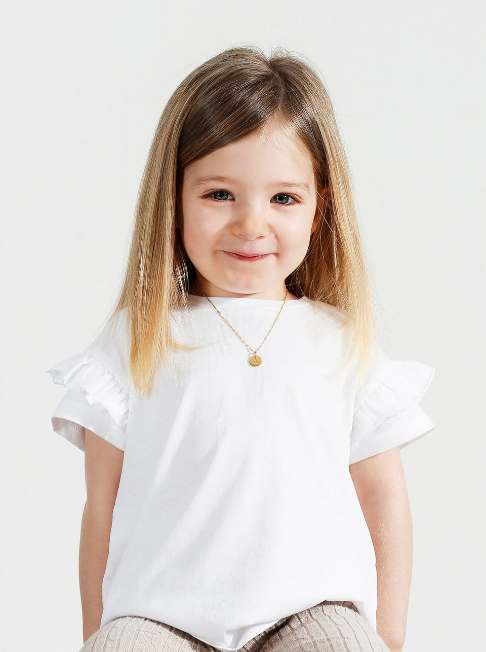 A young girl models the Beloved Baby Chain in gold, styled with a small, round letter A pendant.