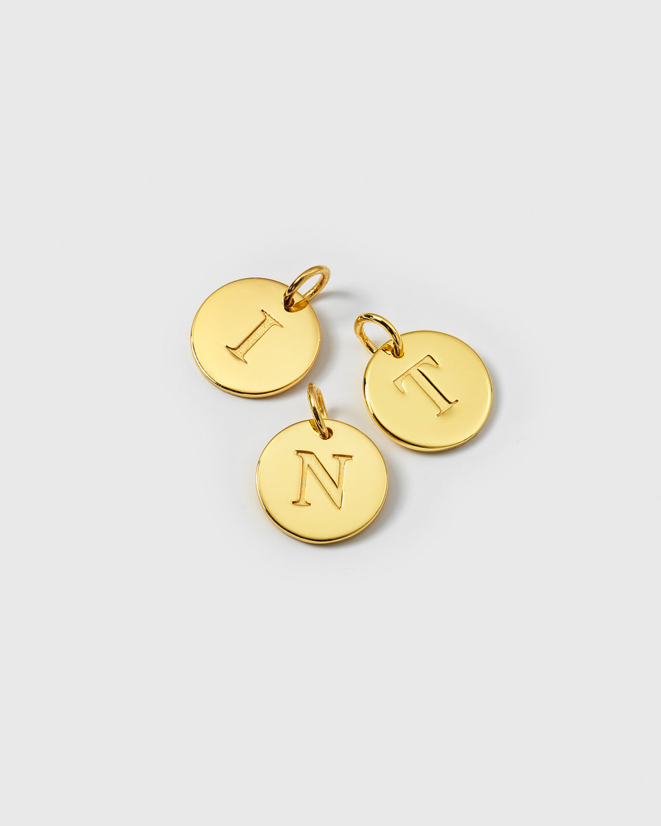 A product shot displaying three of the Beloved Big Letter Gold pendants, featuring the letters I, T, and N.