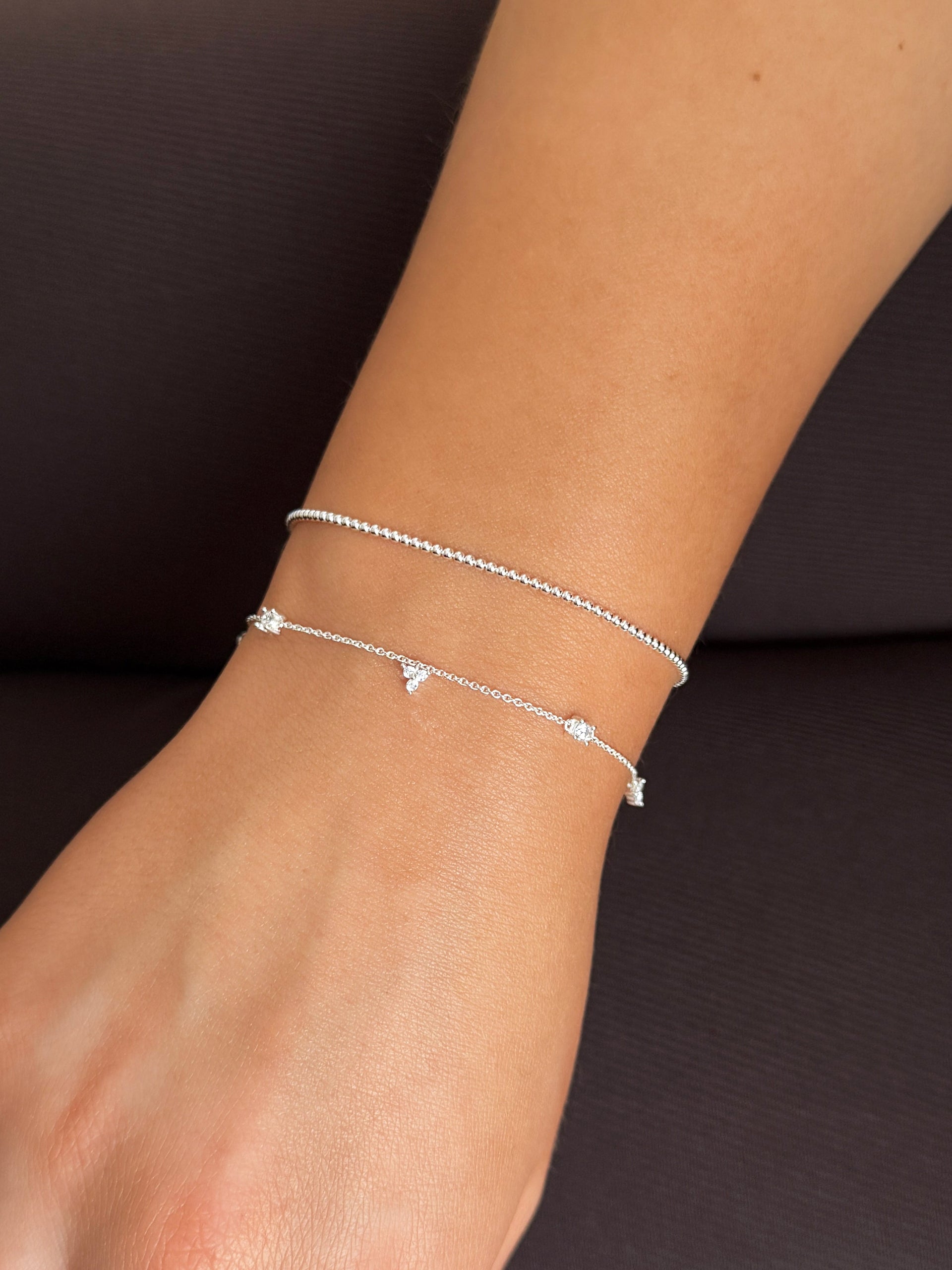 Layered silver bracelets: cubic zirconia chain and thin beaded chain.