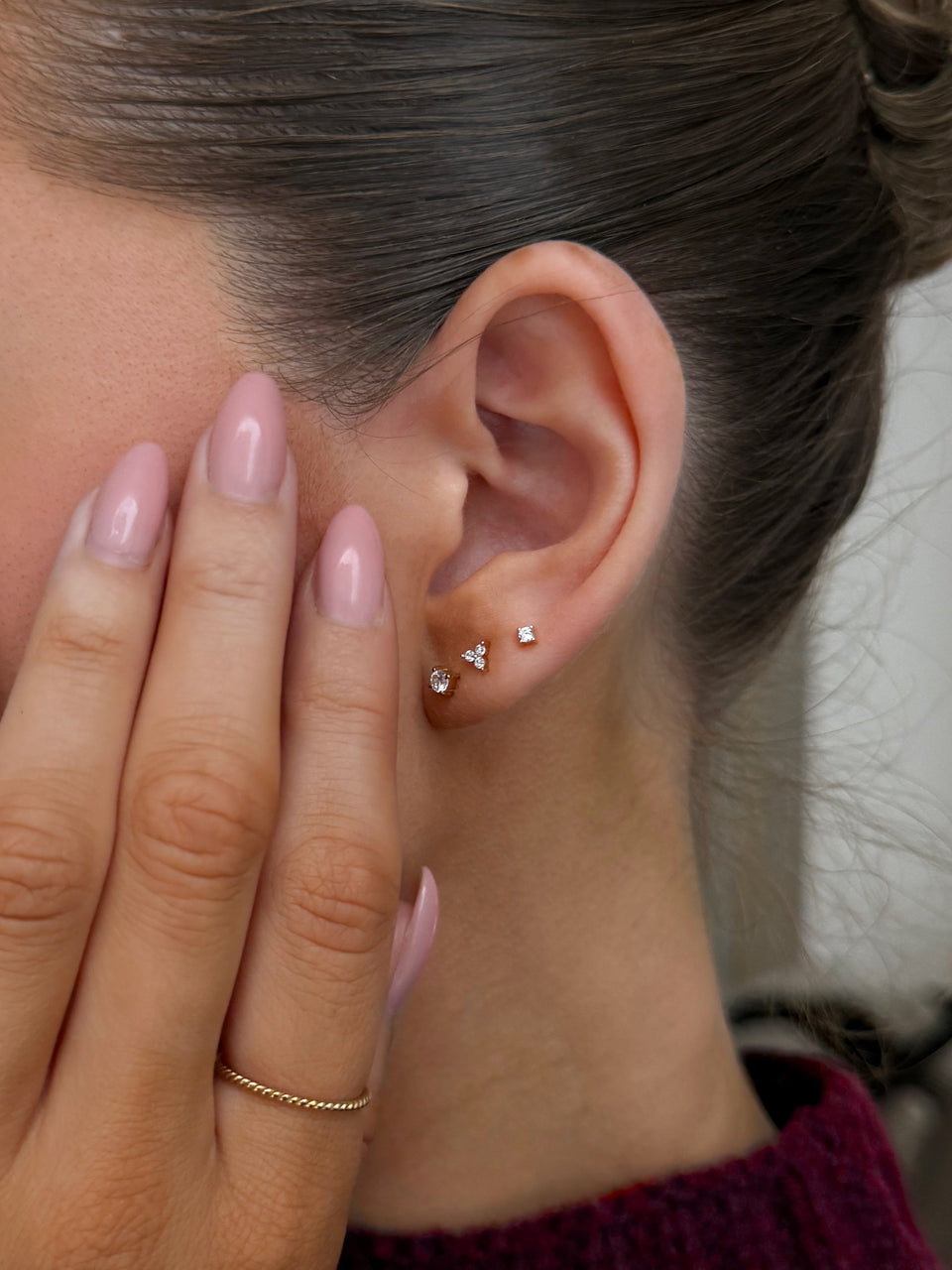 A stack of three gold stud earrings with sparkling stones, paired with a thin twisted gold ring.