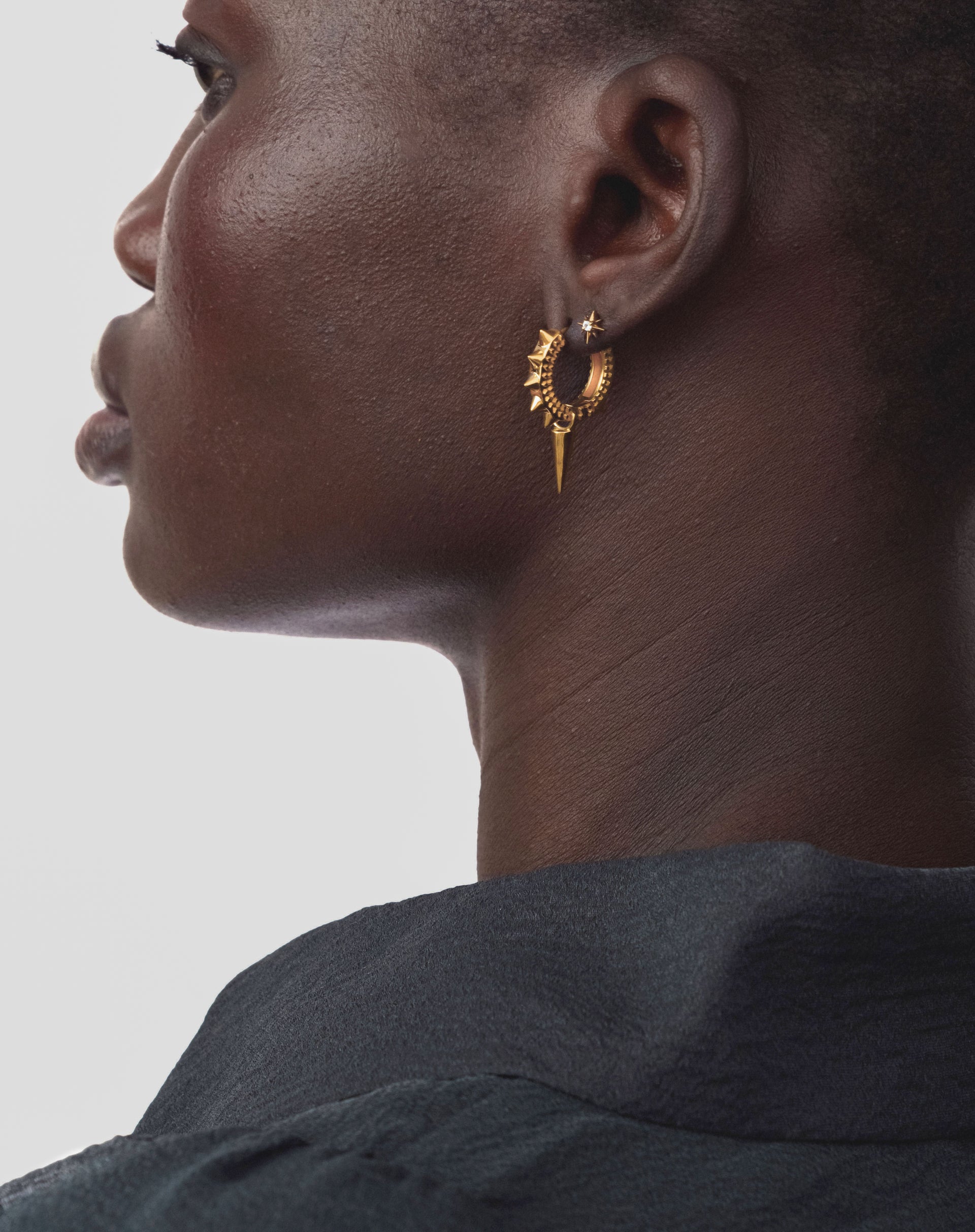 A close-up on a model wearing the gold North Star Stud Earring, featuring a small star with a crystal, styled with a larger, spiky gold hoop earring.