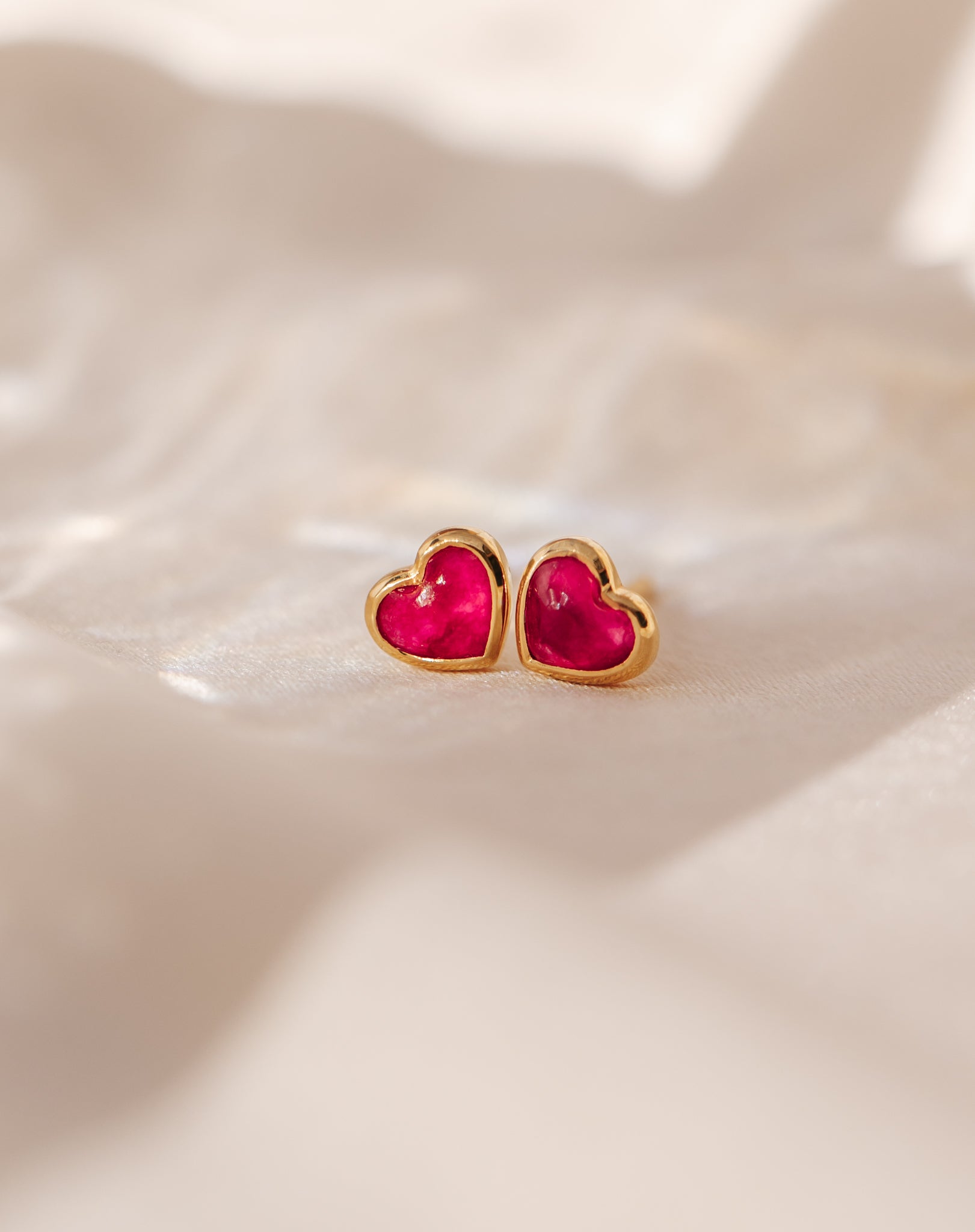 A close-up of the La La Love Studs Gold, a pair of heart-shaped earrings featuring a vibrant pink quartz stone set in a polished gold casing.