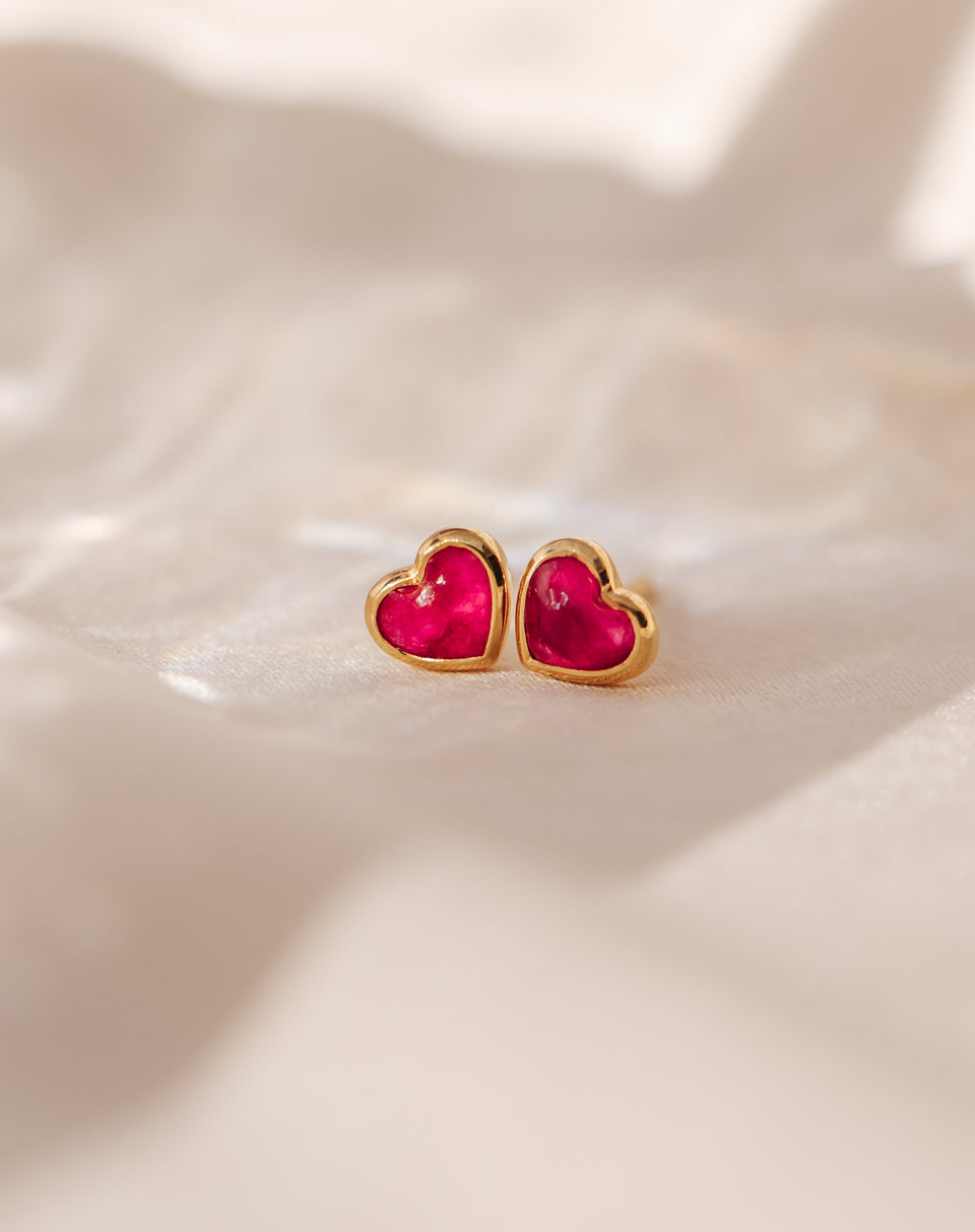 A close-up of the La La Love Studs Gold, a pair of heart-shaped earrings featuring a vibrant pink quartz stone set in a polished gold casing.