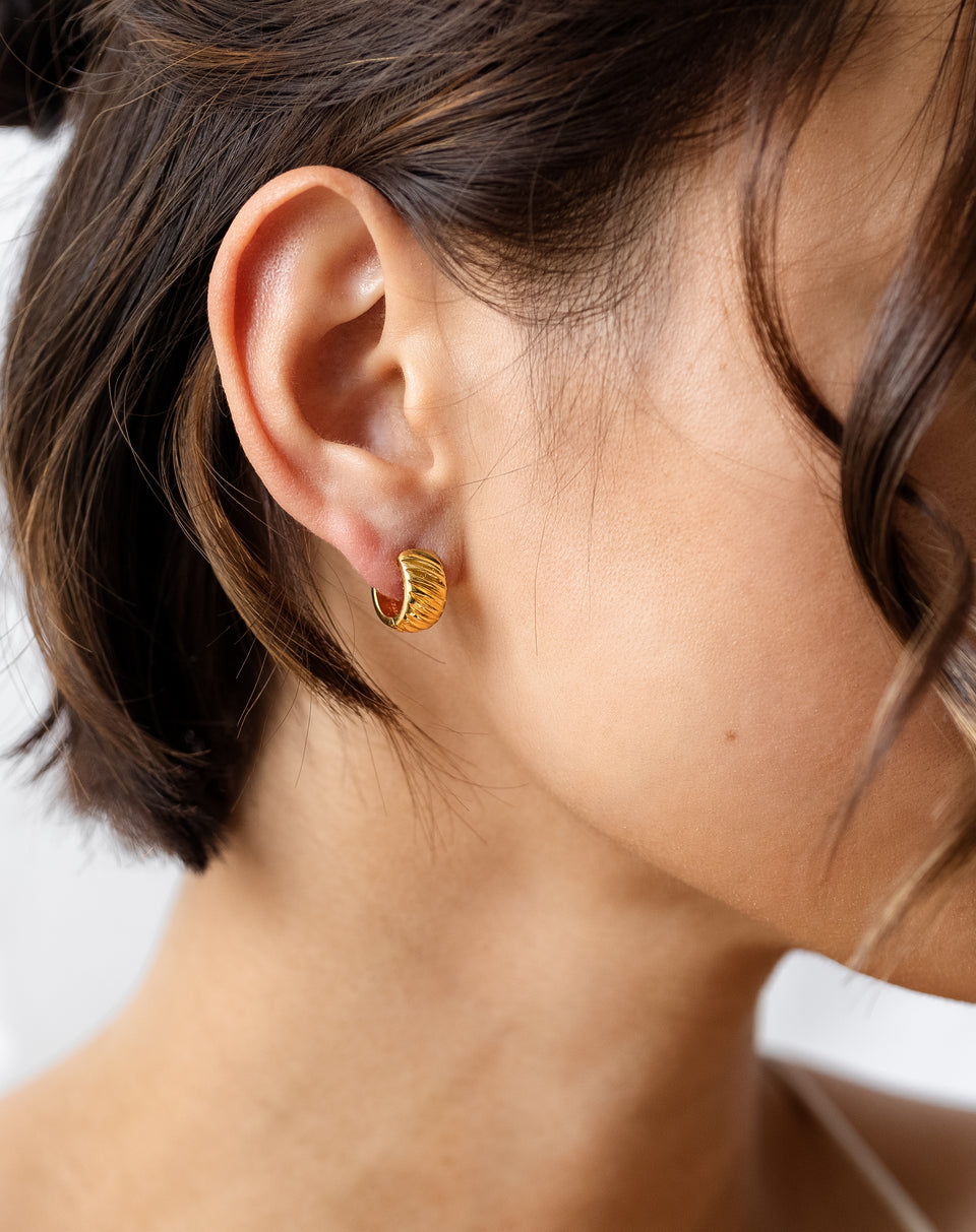 A close-up shot of a model's ear, wearing the chunky La La Love Plain Hoops in gold with a distinct ribbed texture.