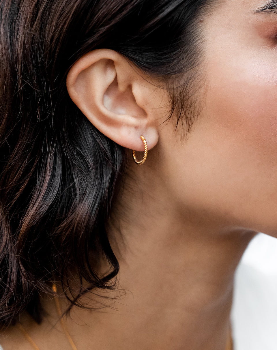 A close-up shot of a model wearing the Beloved Twisted Medium Hoops in gold, showcasing their unique twisted design.