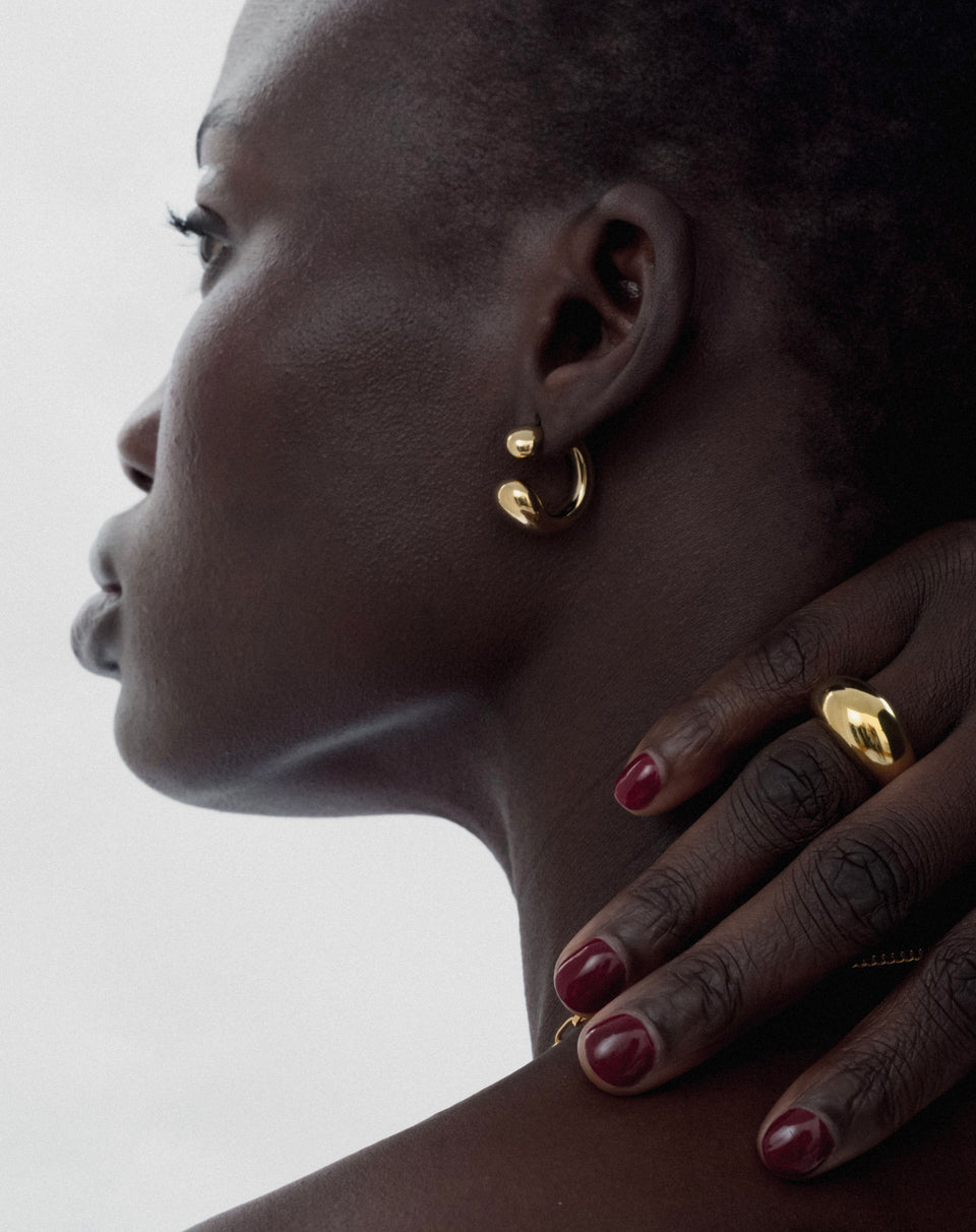 A close-up profile of a model wearing the gold Bolded Drops Earrings, featuring a unique drop shape, paired with a chunky gold dome ring.