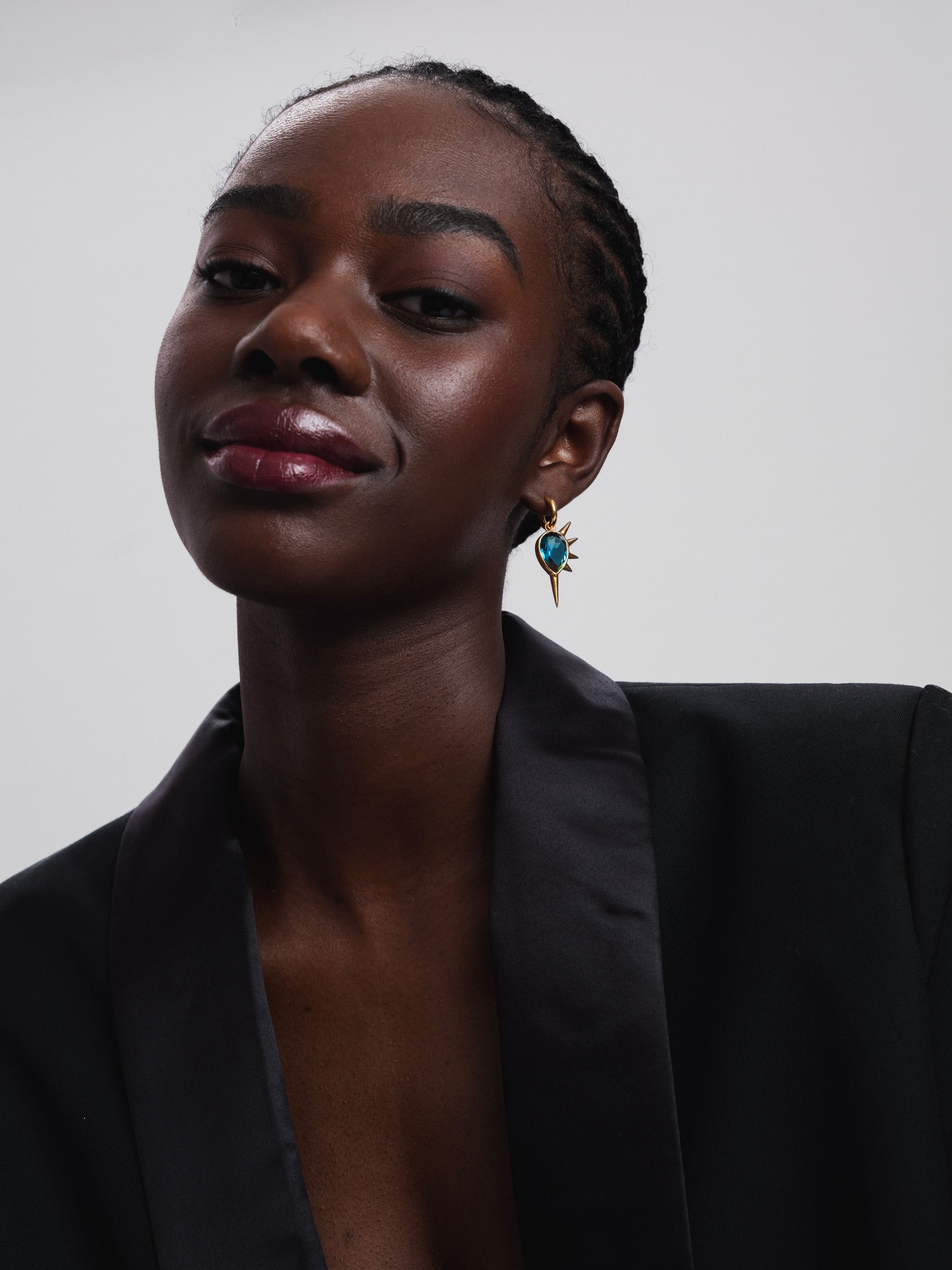 A close-up shot of a model wearing the Queen Of Spikes Earring in gold, highlighting its dangling design with a large teal quartz stone and bold spikes.