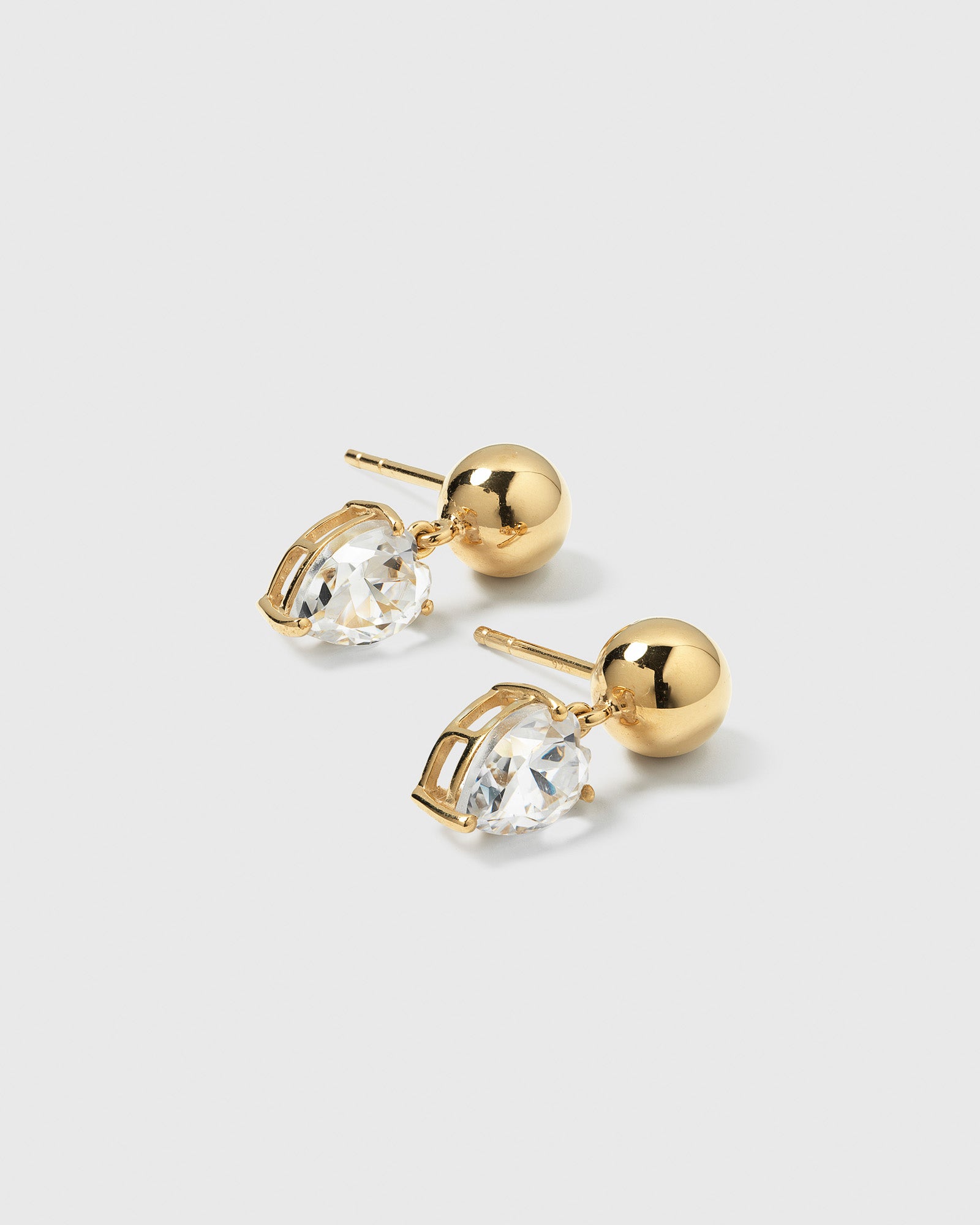 A product shot of the Katie Earrings in gold, featuring a gold sphere stud with a dangling drop-shaped cubic zirconia.