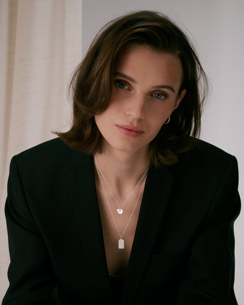 A delicate silver star pendant layered with a longer necklace featuring a rectangular pendant, paired with small silver hoop earrings.