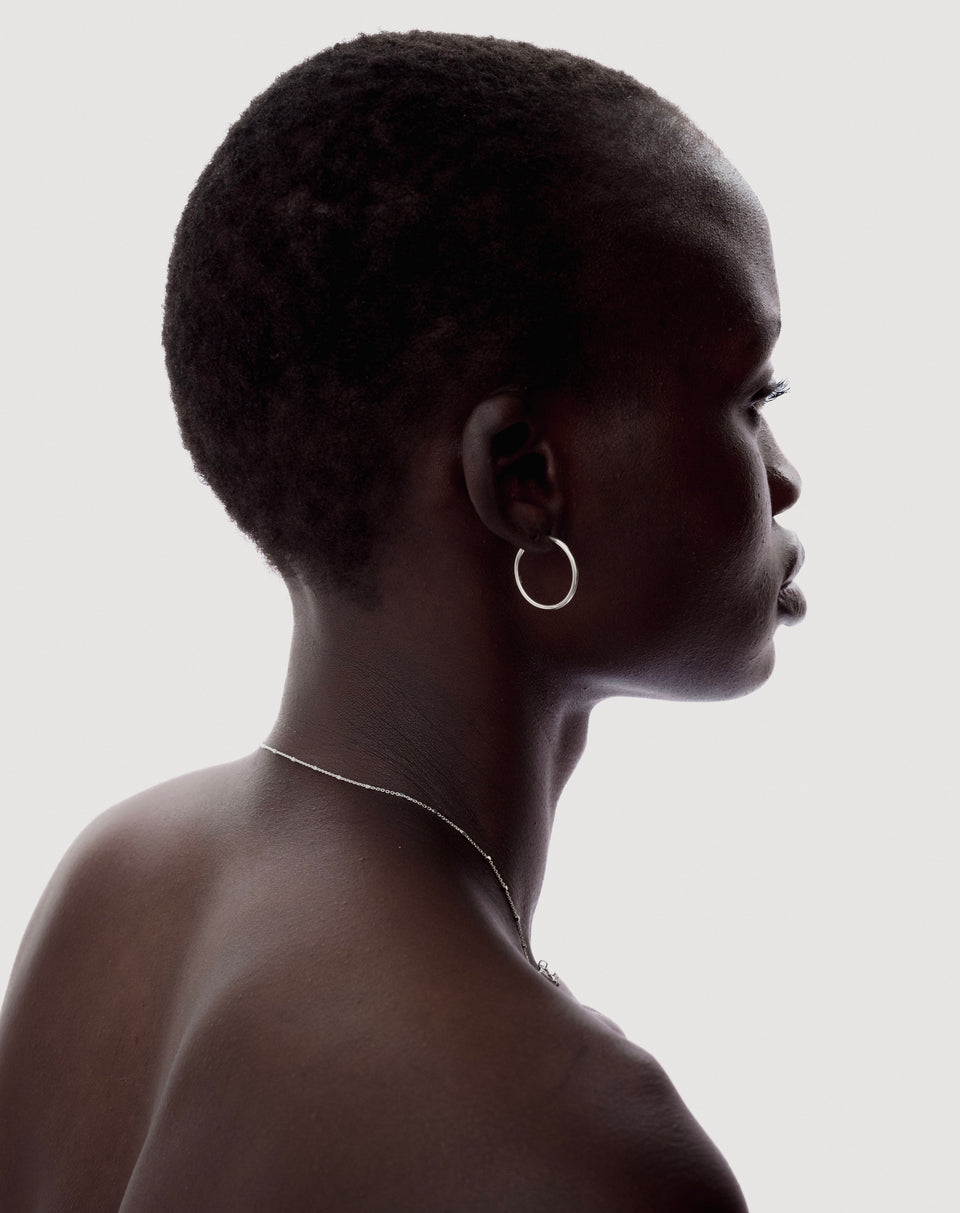 A close-up profile of a model wearing the Beloved Medium Hoops in silver and a thin silver chain necklace.