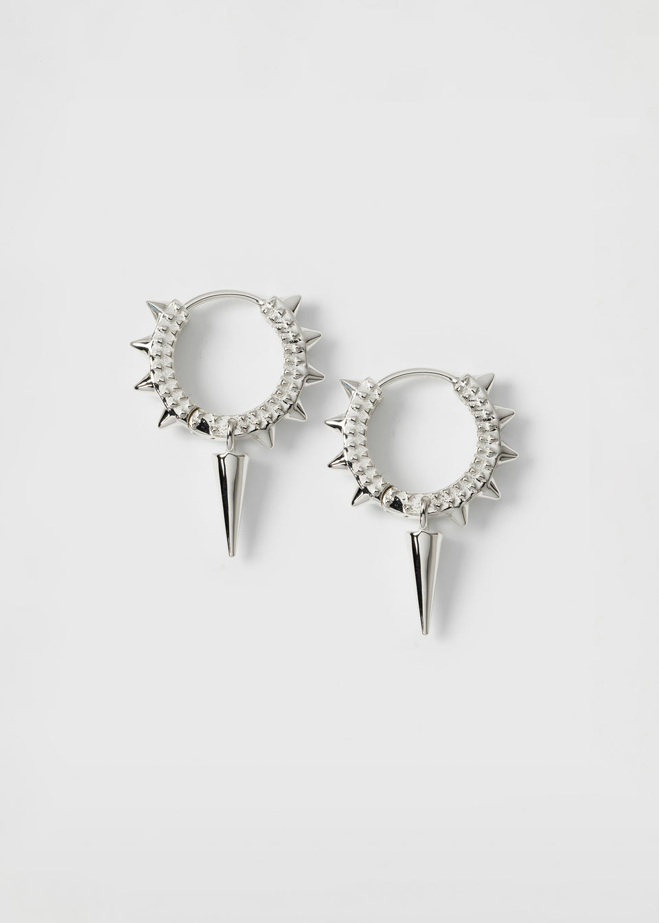 A product shot of the silver Harvey Heavy Spike Hoops, featuring a pair of textured hoops with small spikes along the outer edge and a larger, dangling spike charm on each earring.