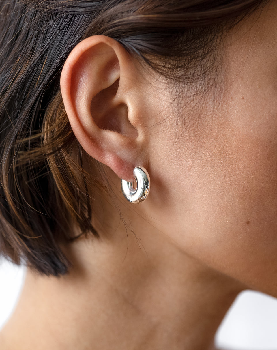 A close-up shot of a model wearing the Bolded Little Sis Hoops in silver, showcasing their chunky, rounded design.