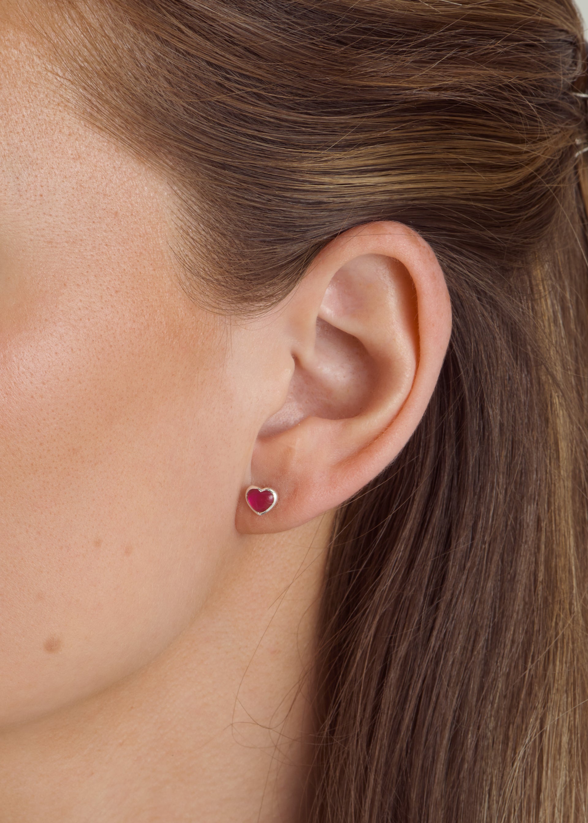 Close-up of a model wearing the La La Love stud earring, a small heart-shaped design featuring a pink quartz stone set in sterling silver.
