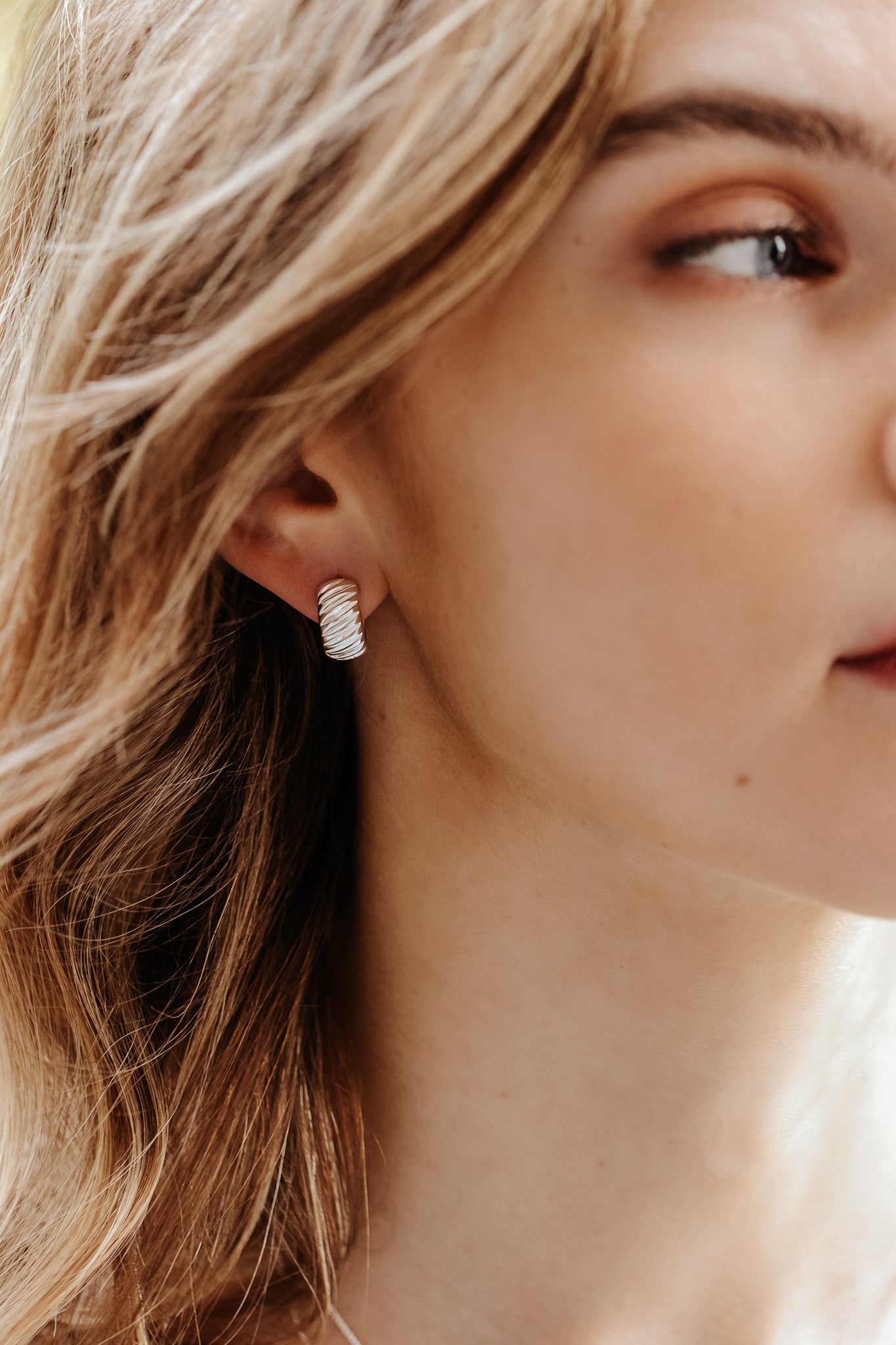 A close-up of a model wearing the chunky La La Love Plain Hoops in silver, highlighting the ribbed texture of the earring.