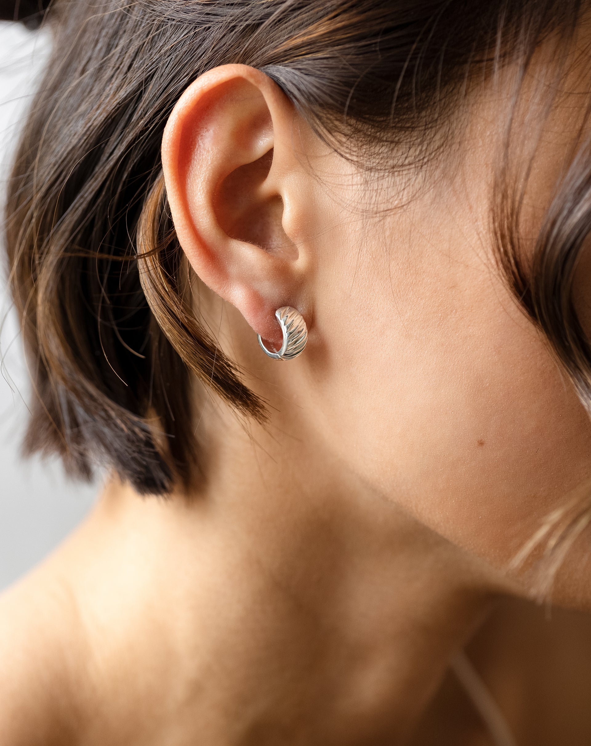 A close-up view of the La La Love Plain Hoops in silver worn on a model's ear, highlighting the chunky design and ribbed finish.