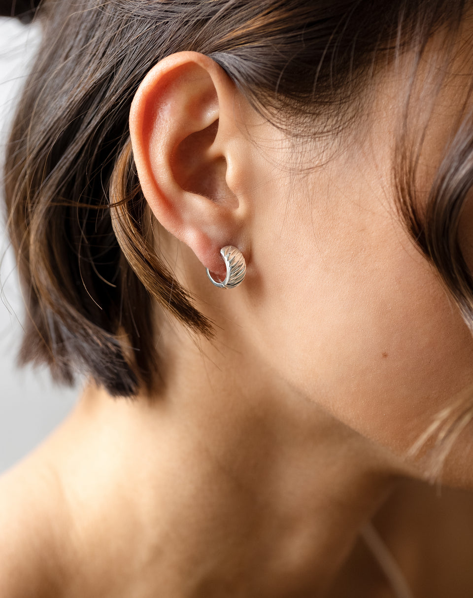A close-up view of the La La Love Plain Hoops in silver worn on a model's ear, highlighting the chunky design and ribbed finish.