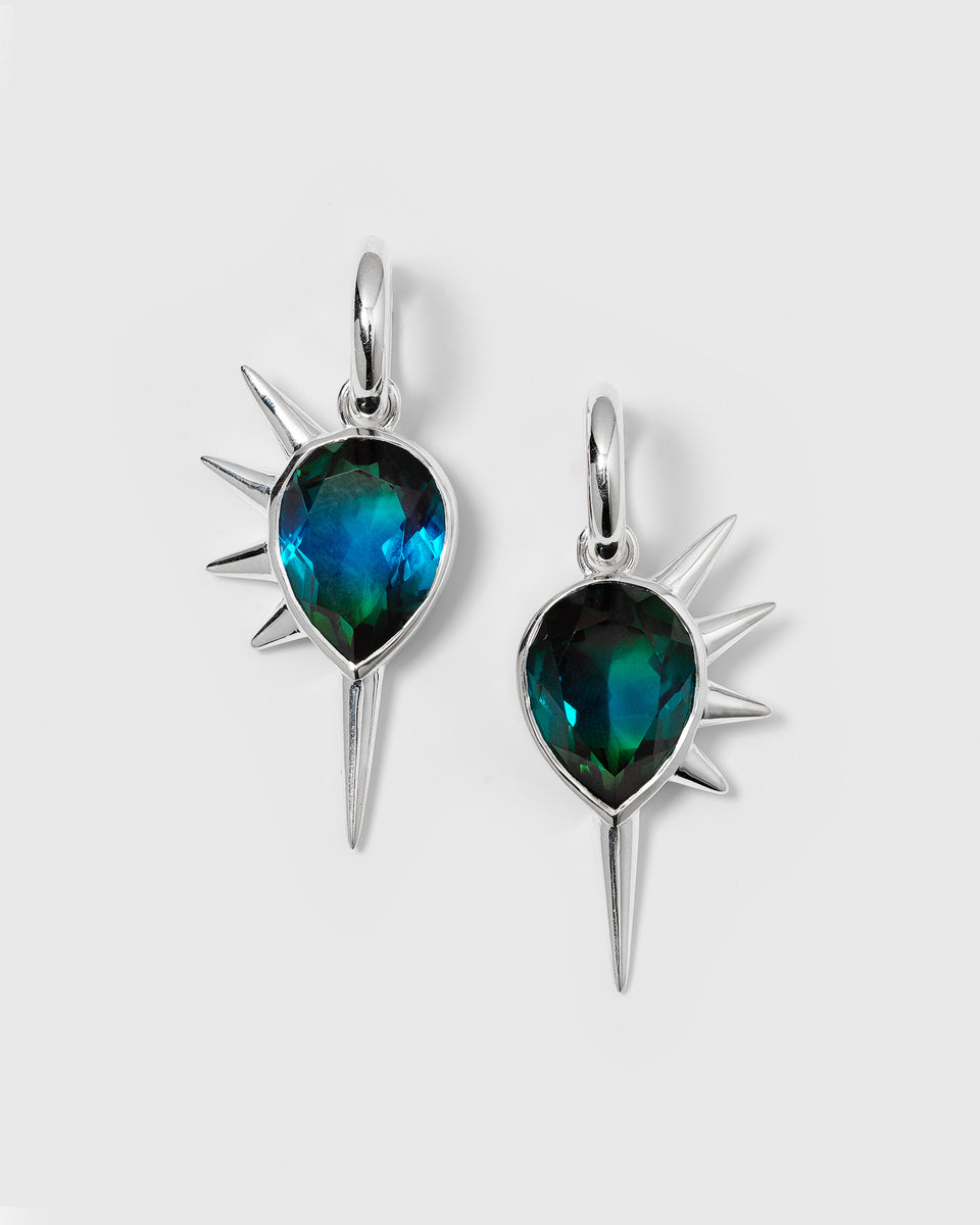 A product shot of the Queen Of Spikes Earrings in silver, featuring a bold design with a large, teardrop-shaped teal quartz stone and decorative silver spikes.